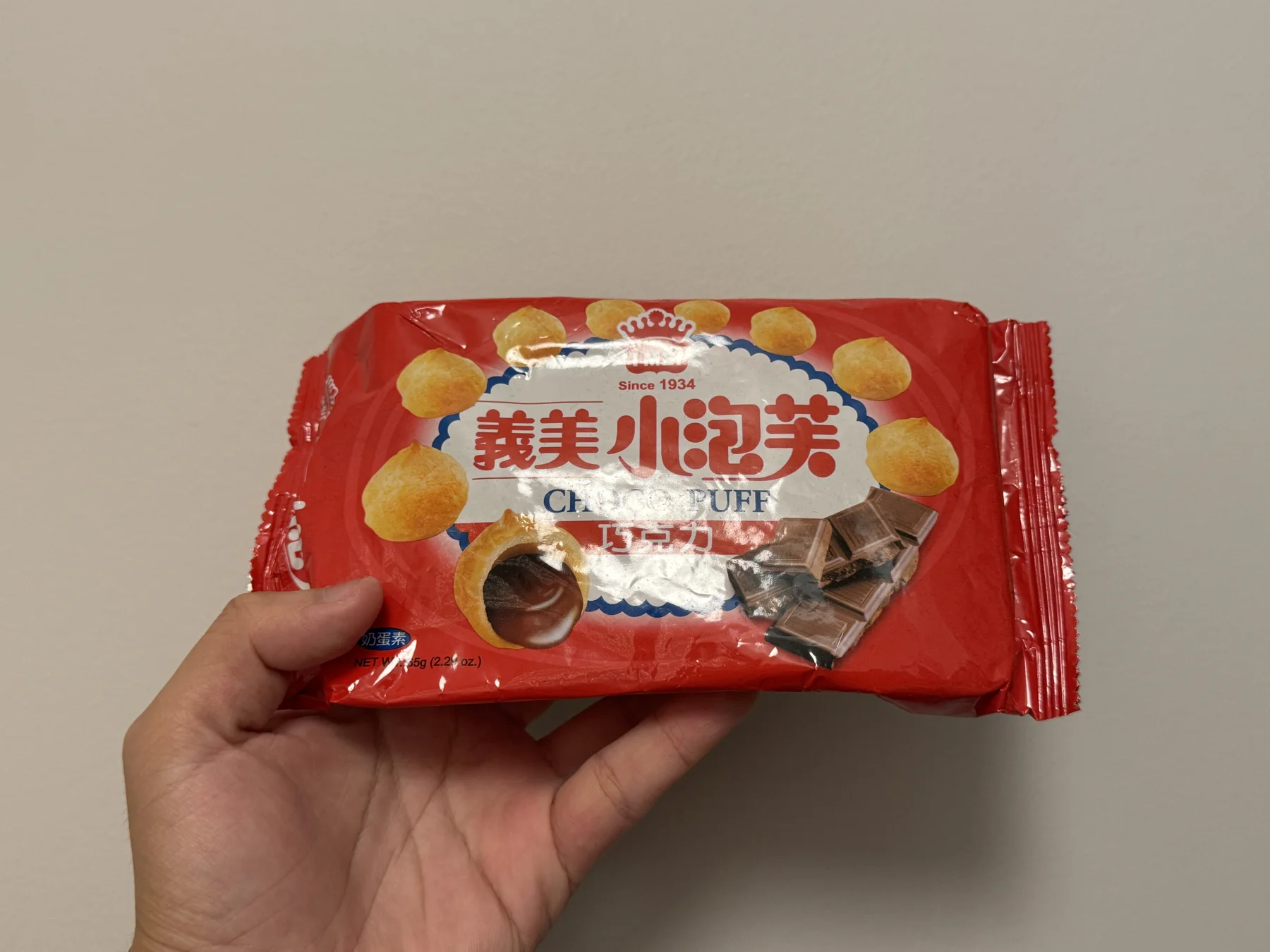 A hand holding a red package of I-Mei chocolate mini puffs, front side