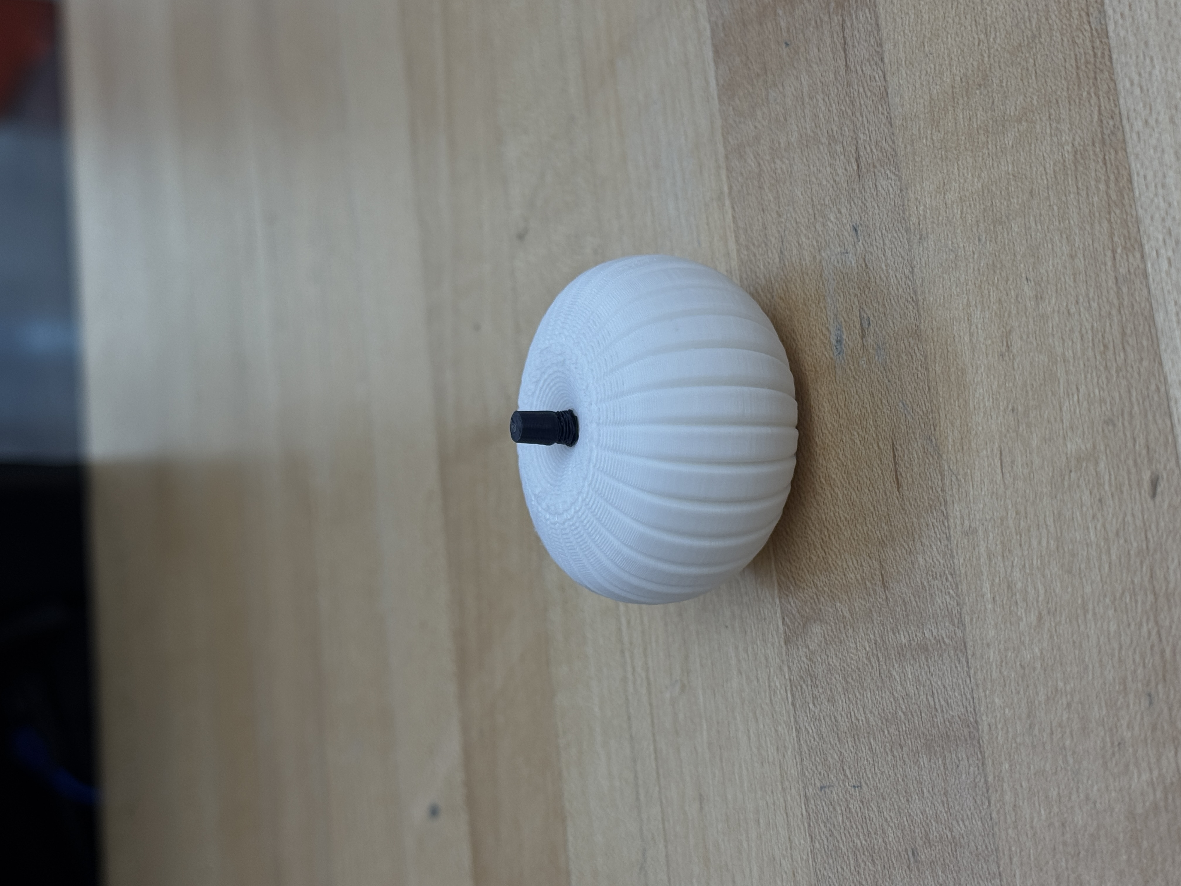 White 3D printed pumpkin with a dark stem on a table.