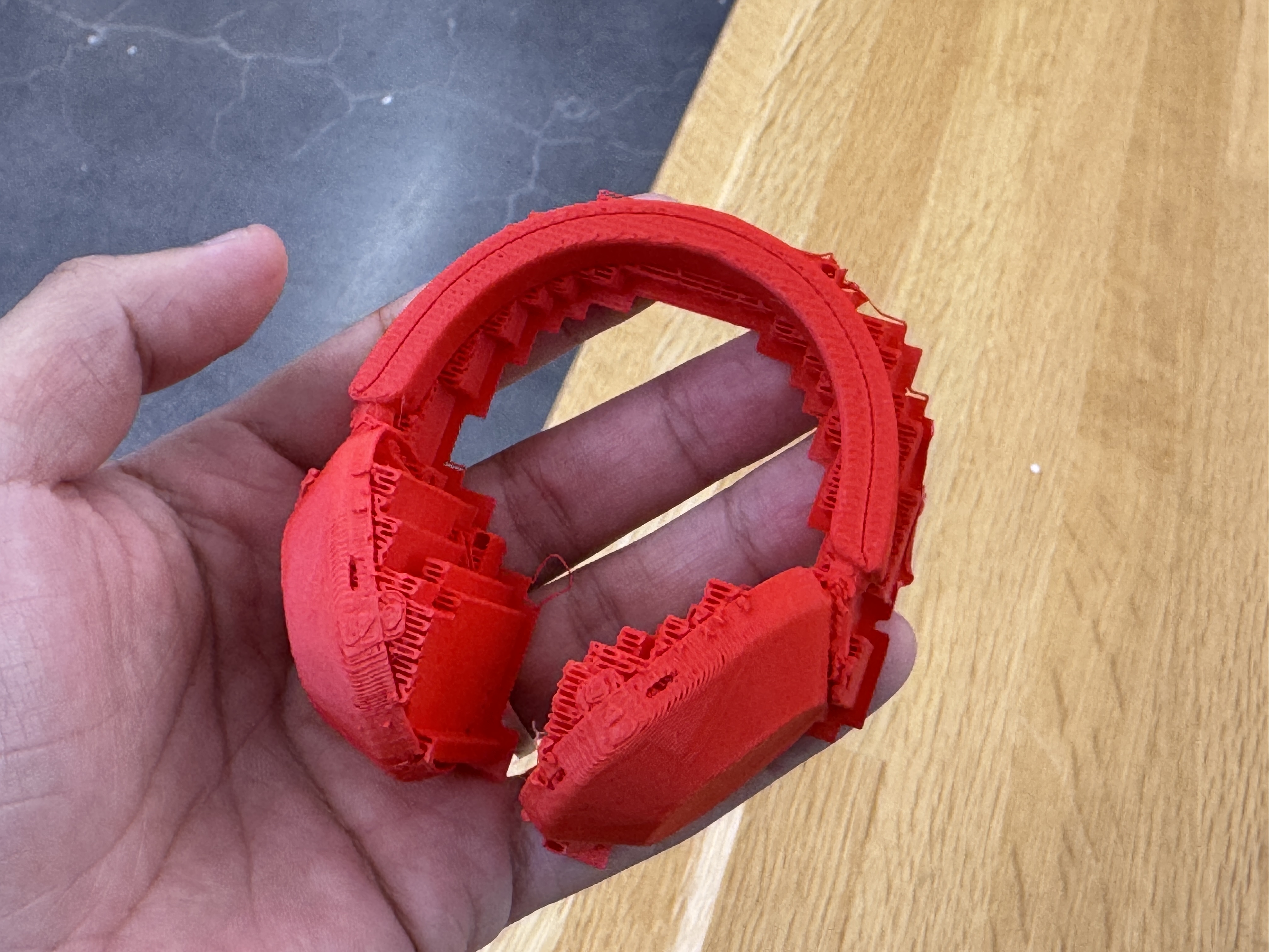 Red 3D printed headphones held in a hand, with support material still attached.