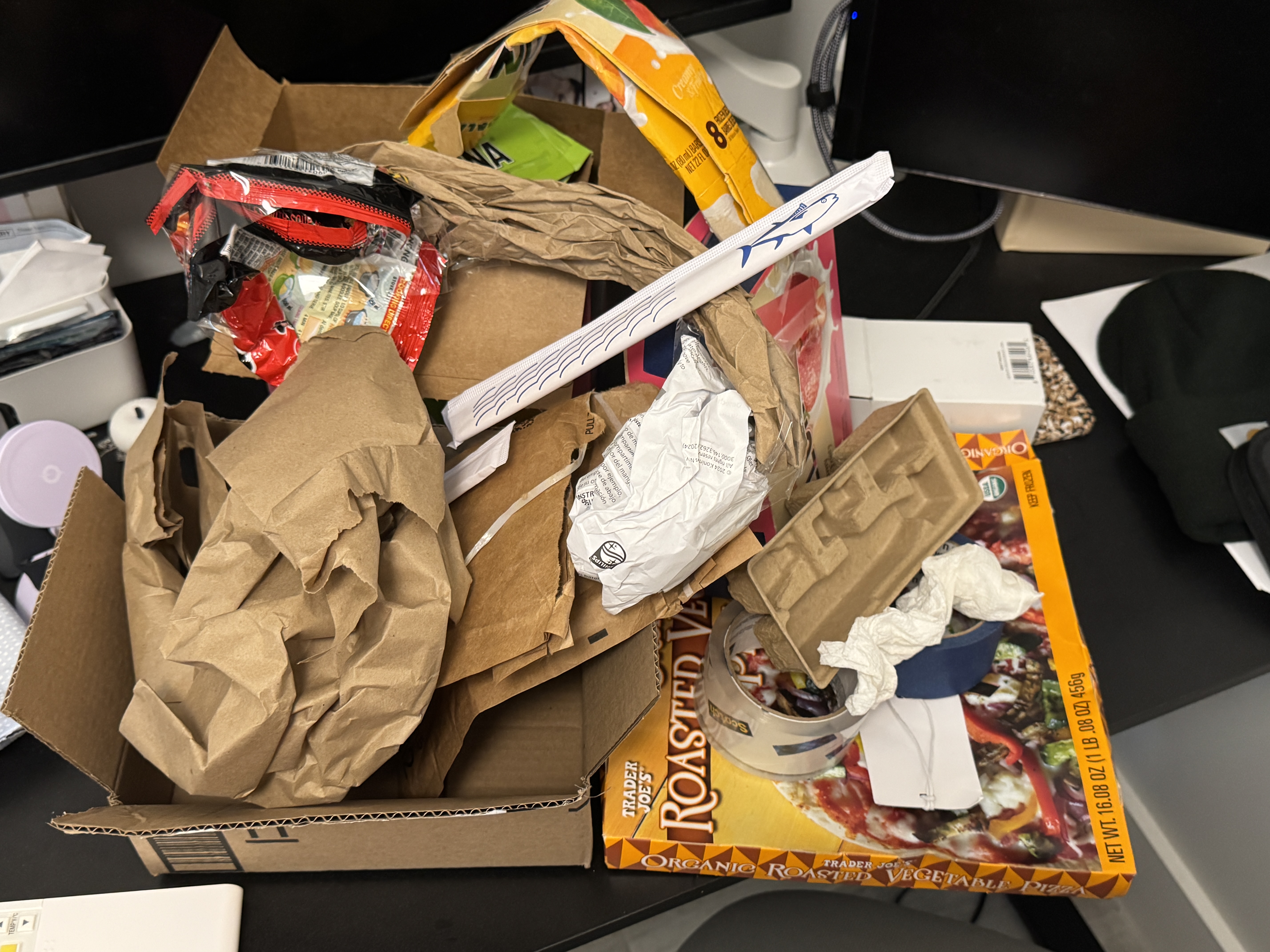 Discarded cardboard, paper packaging, plastic food packaging, and other collected materials piled on a table.