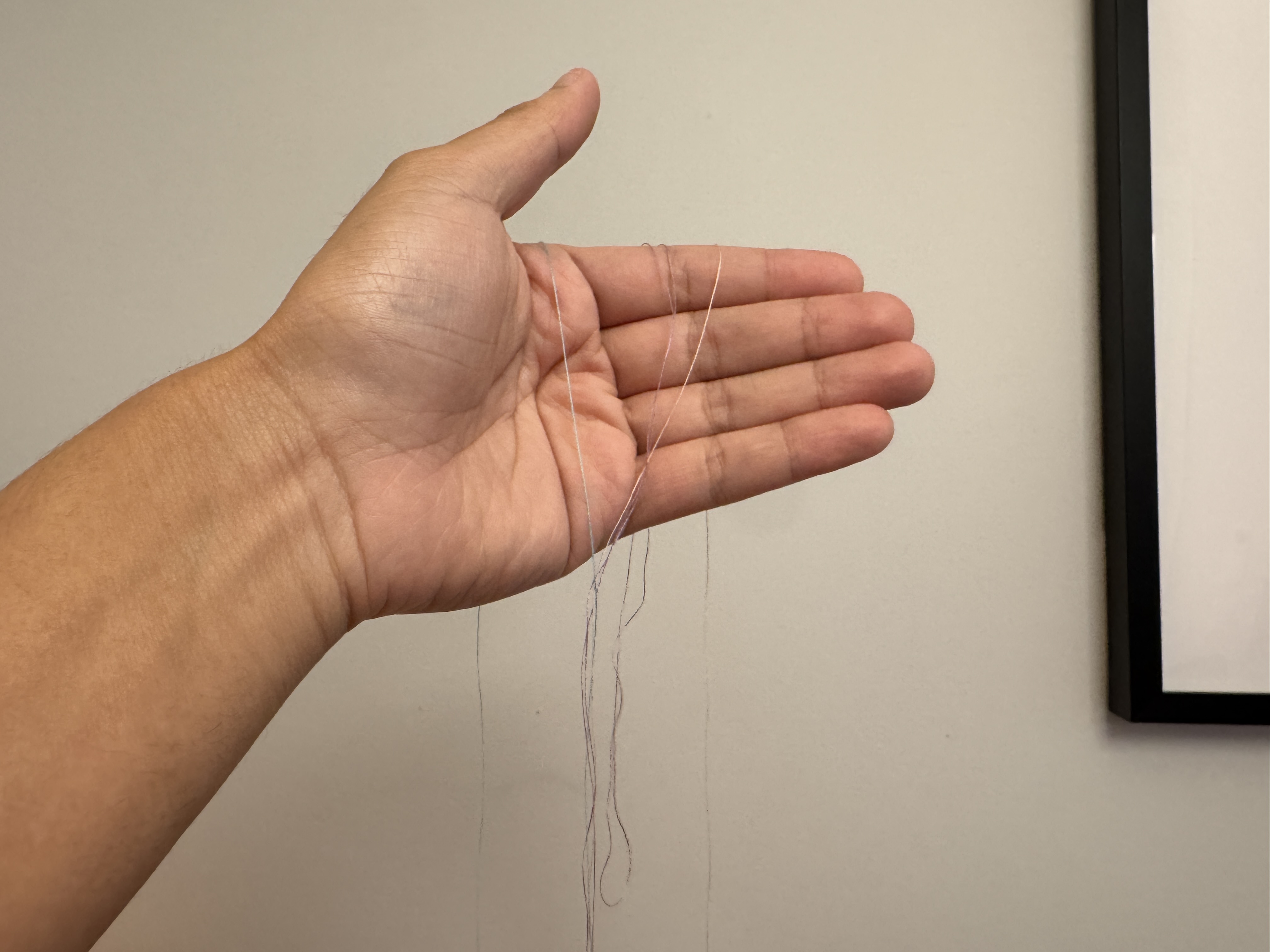 Thin colored threads hanging across an open hand.
