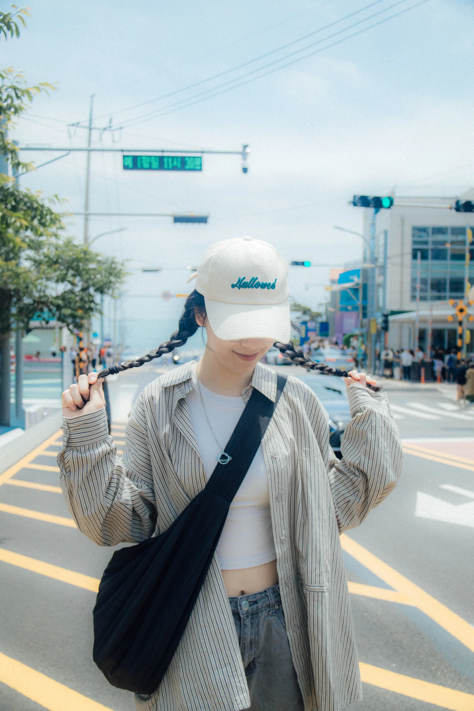 A person wearing a white cap and shoulder bag walks along a sunny city street.