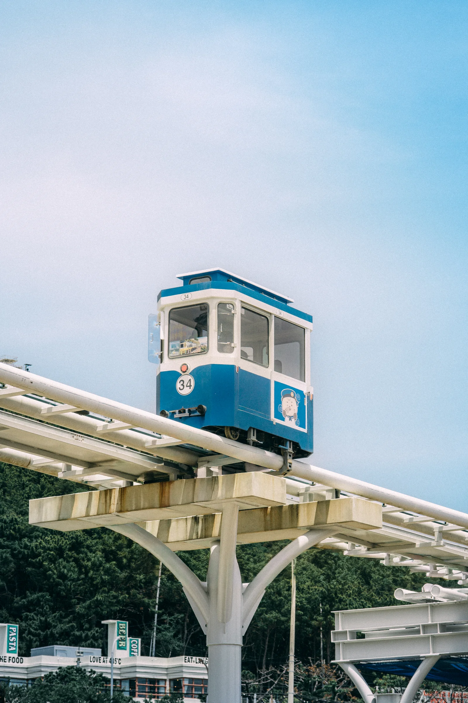 A blue and cream sky capsule travels along an elevated track against a bright blue sky.
