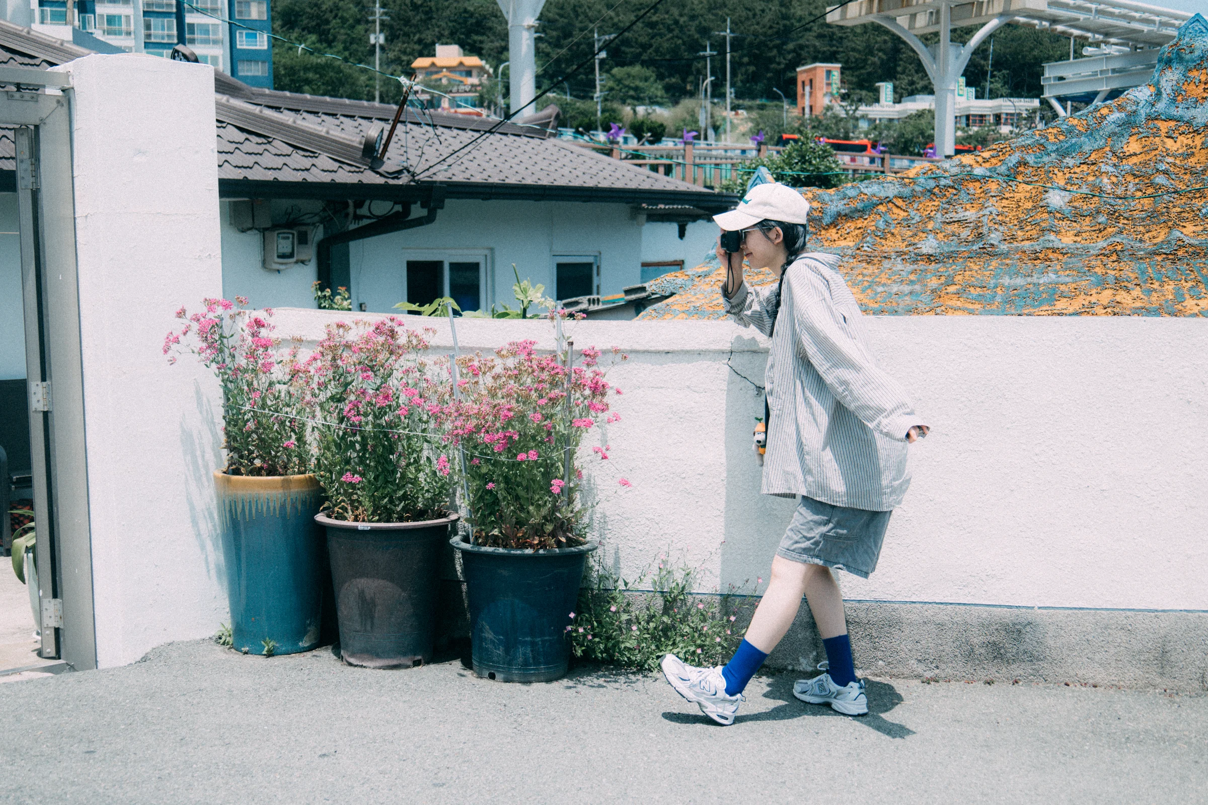 A person walks past pots of flowers and low walls along a neighborhood lane.