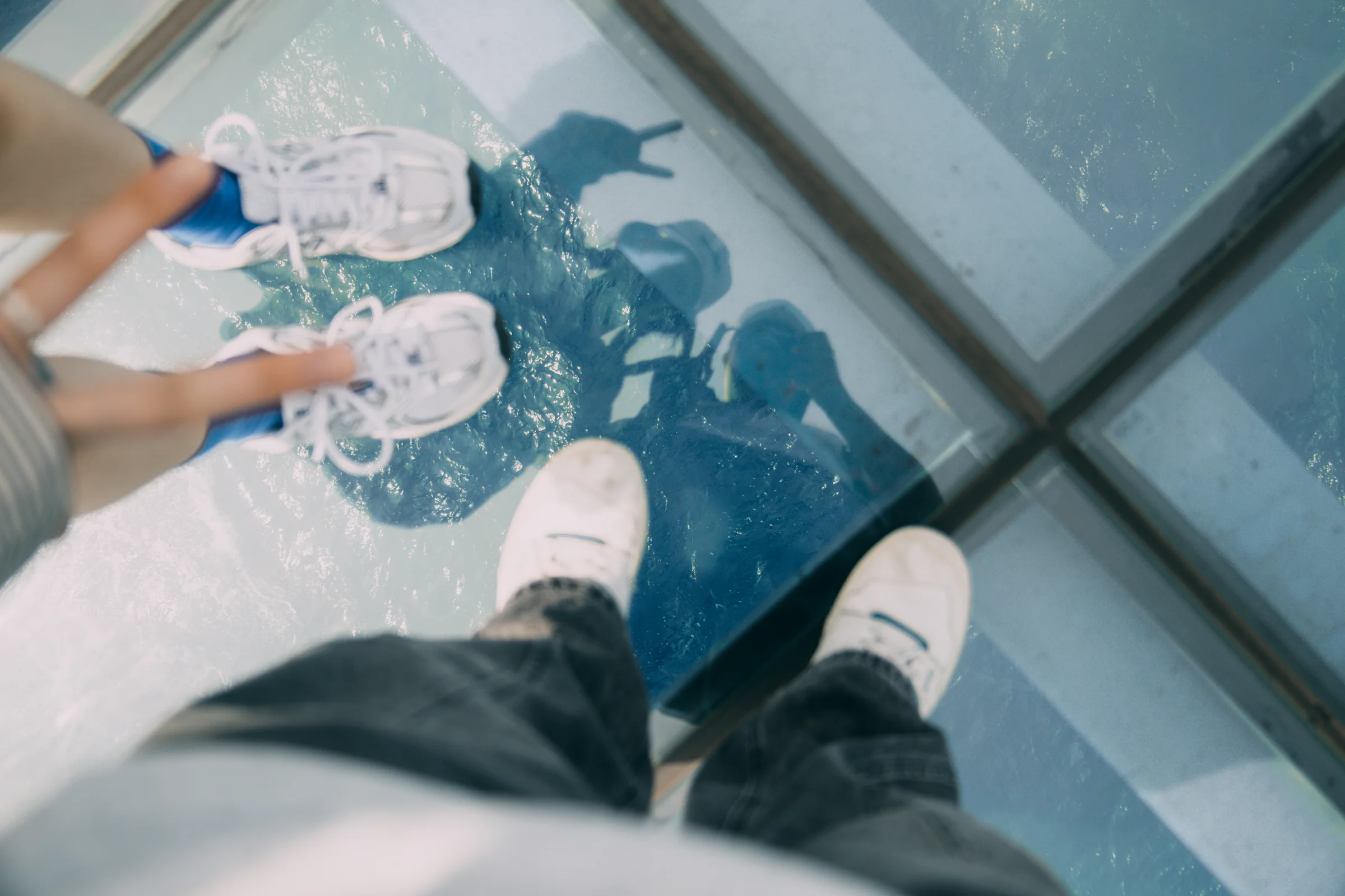 Shoes and legs are reflected in glass floor panels overlooking the water below.