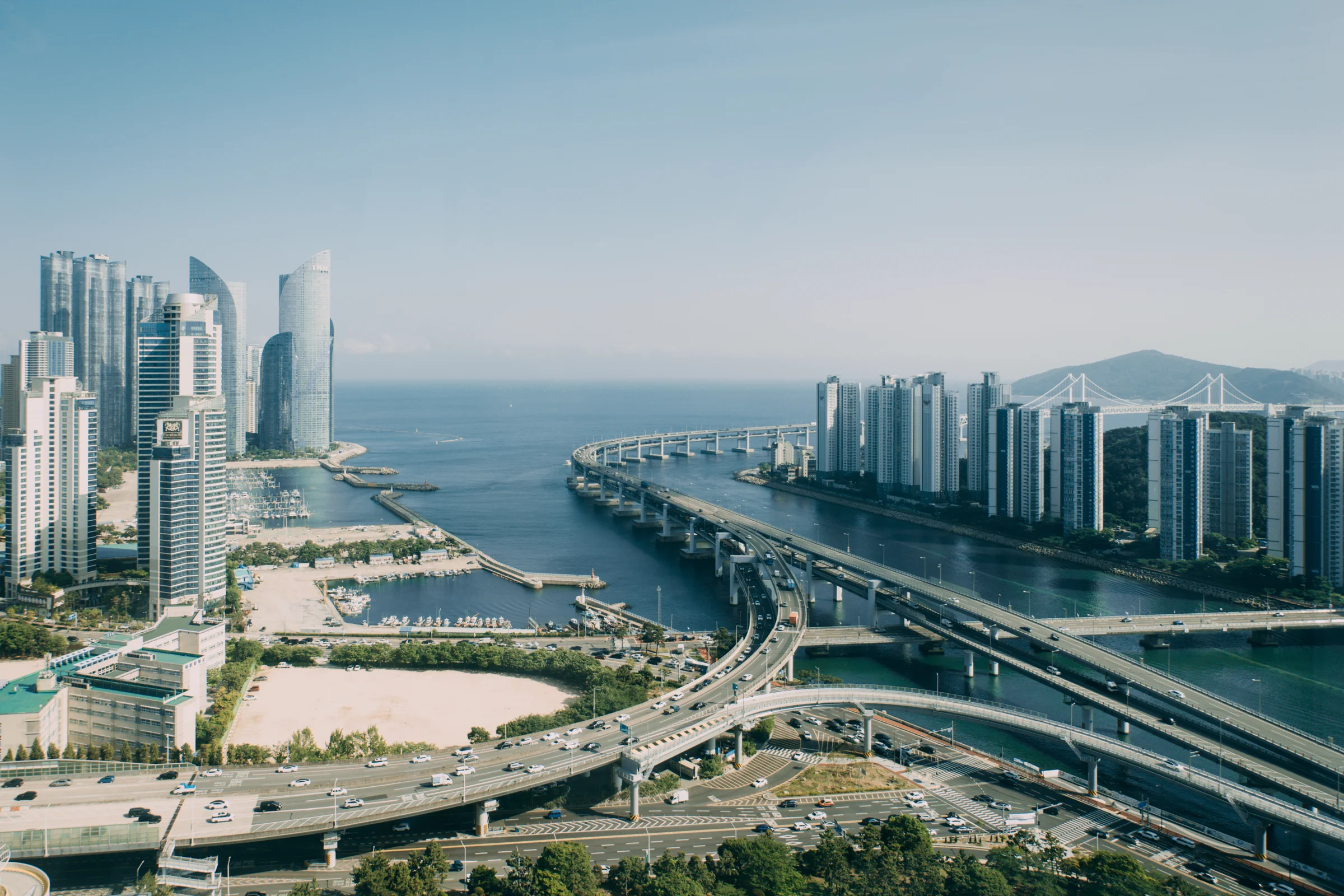 High-rise buildings and curving roads line a waterway opening toward the blue sea.
