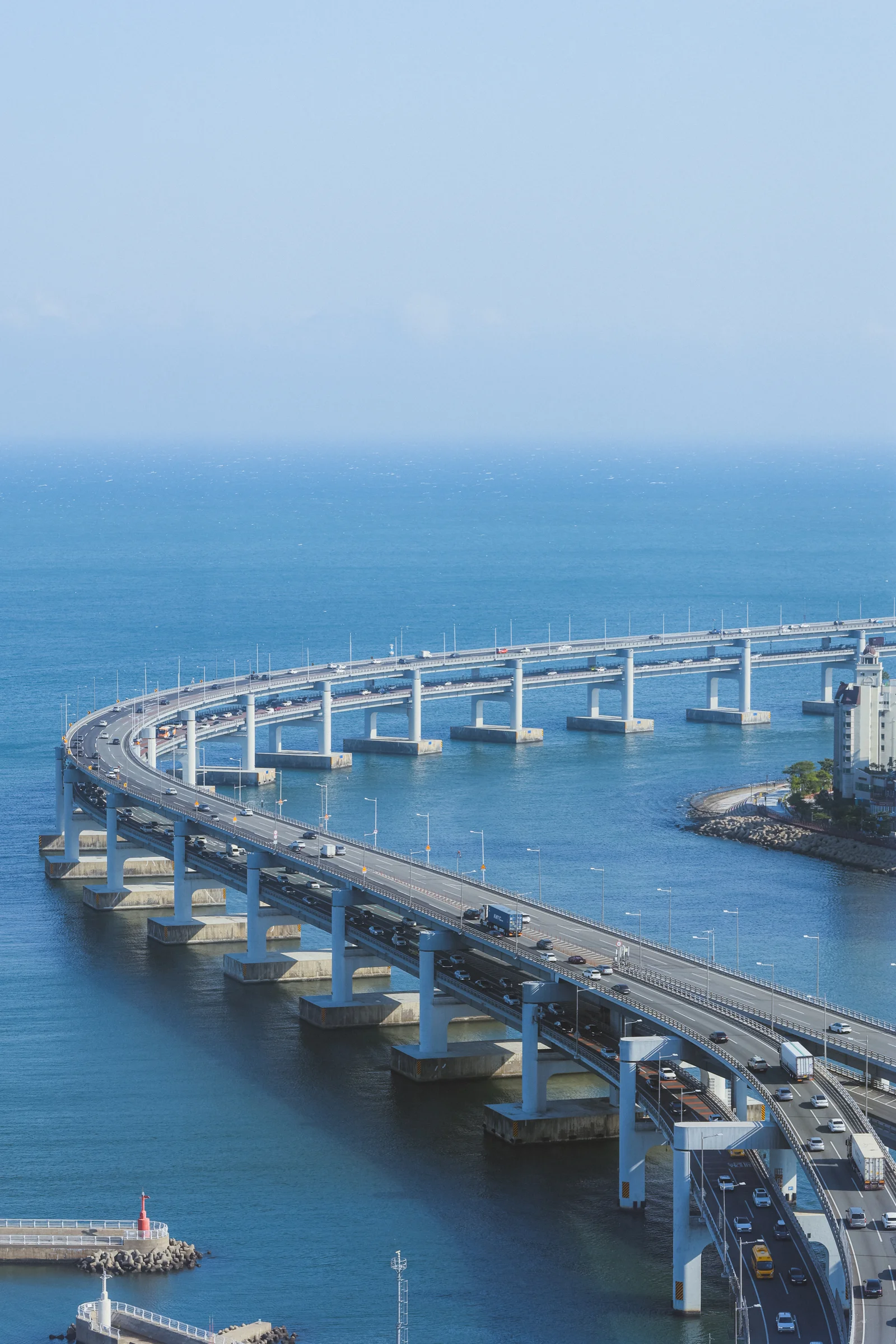An elevated bridge curves across blue water beneath a hazy sky.