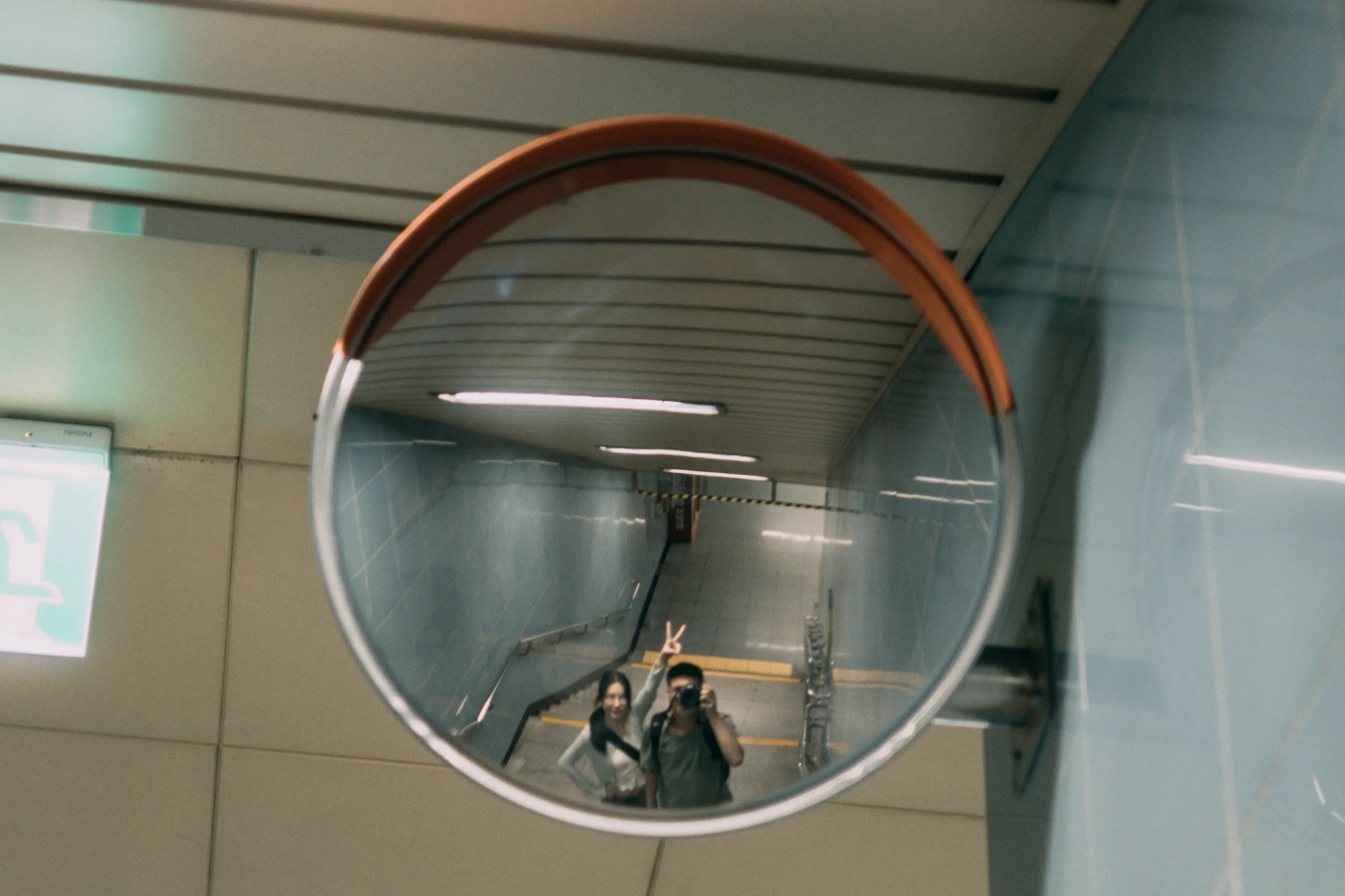 A round convex mirror reflects people beneath an indoor ceiling.