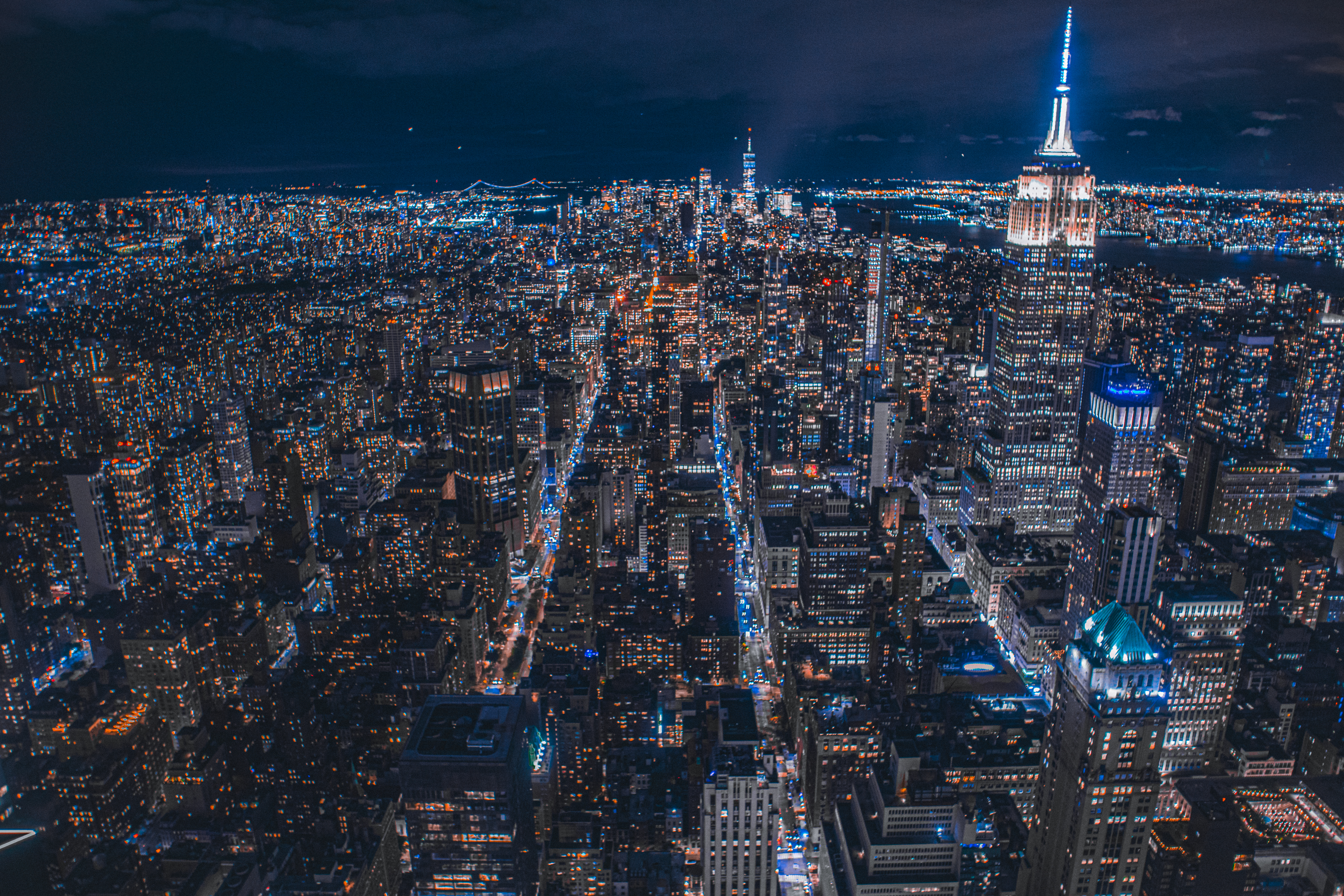An expansive Manhattan skyline at night, with the Empire State Building illuminated in blue.