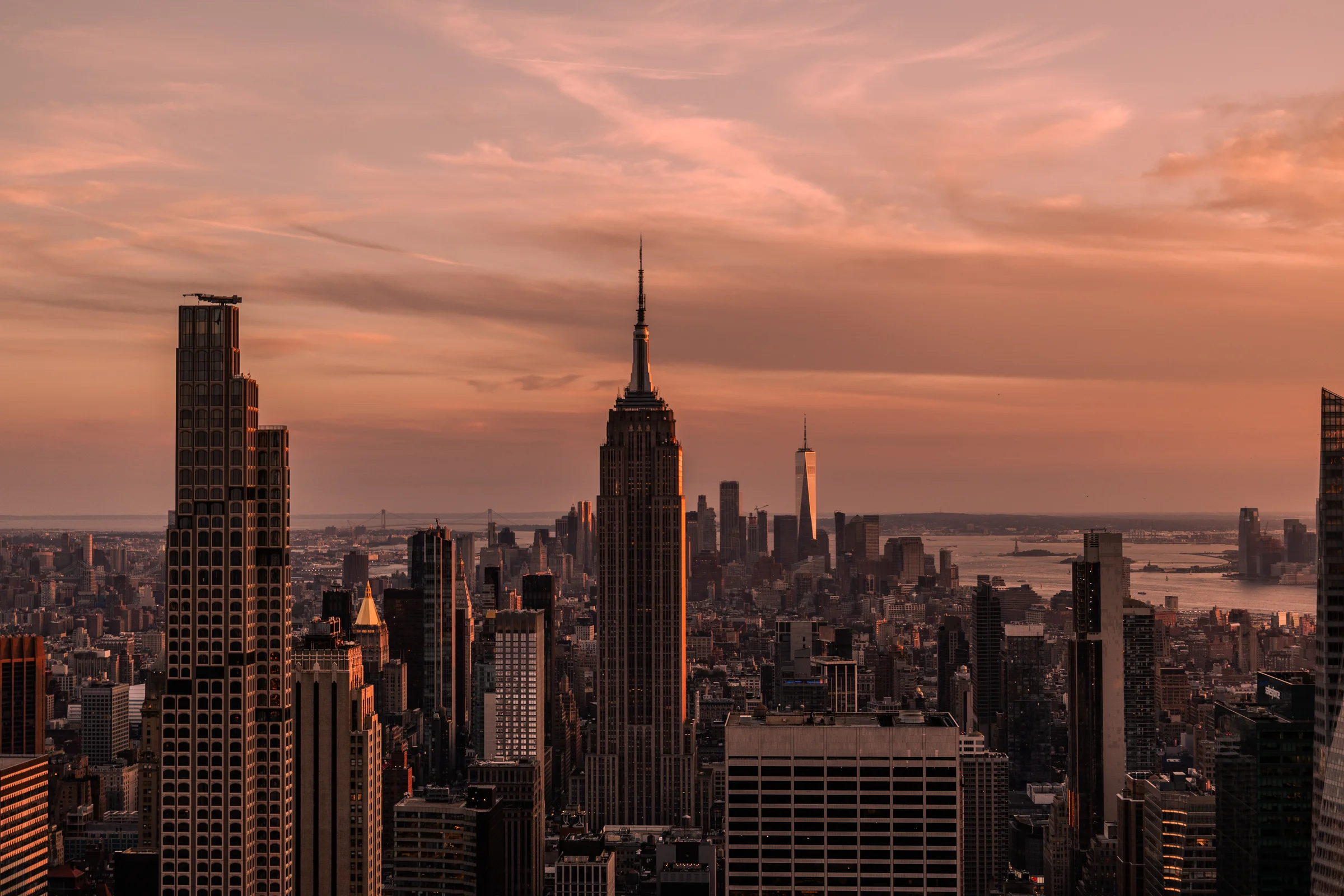 The Empire State Building and Manhattan skyline beneath a pink and orange evening sky.