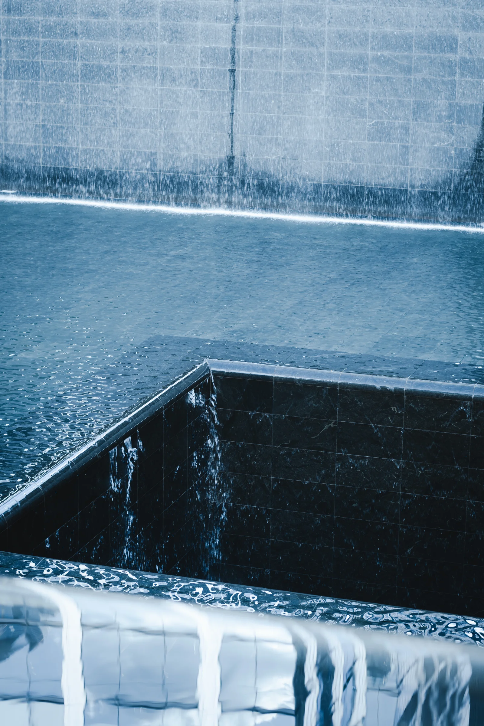 Water cascades into a dark square opening at 911 memorial pools