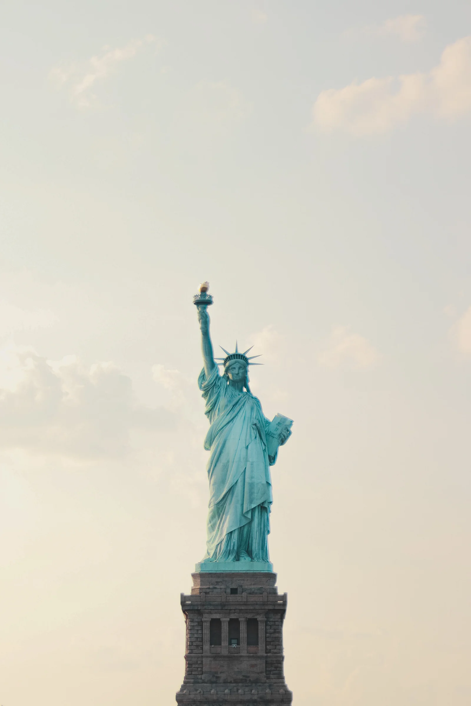 The Statue of Liberty seen against a pale, softly clouded sky.