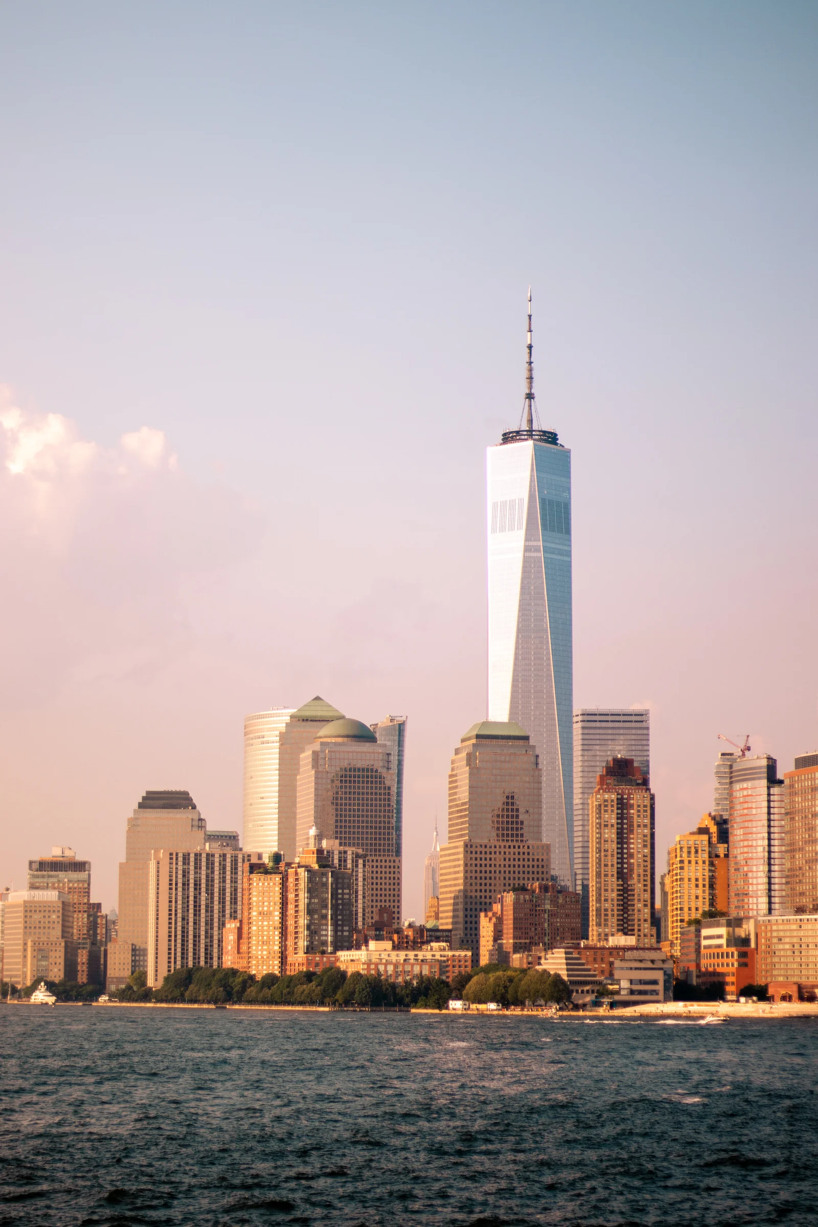 One World Trade Center rises above the Lower Manhattan waterfront in warm light.