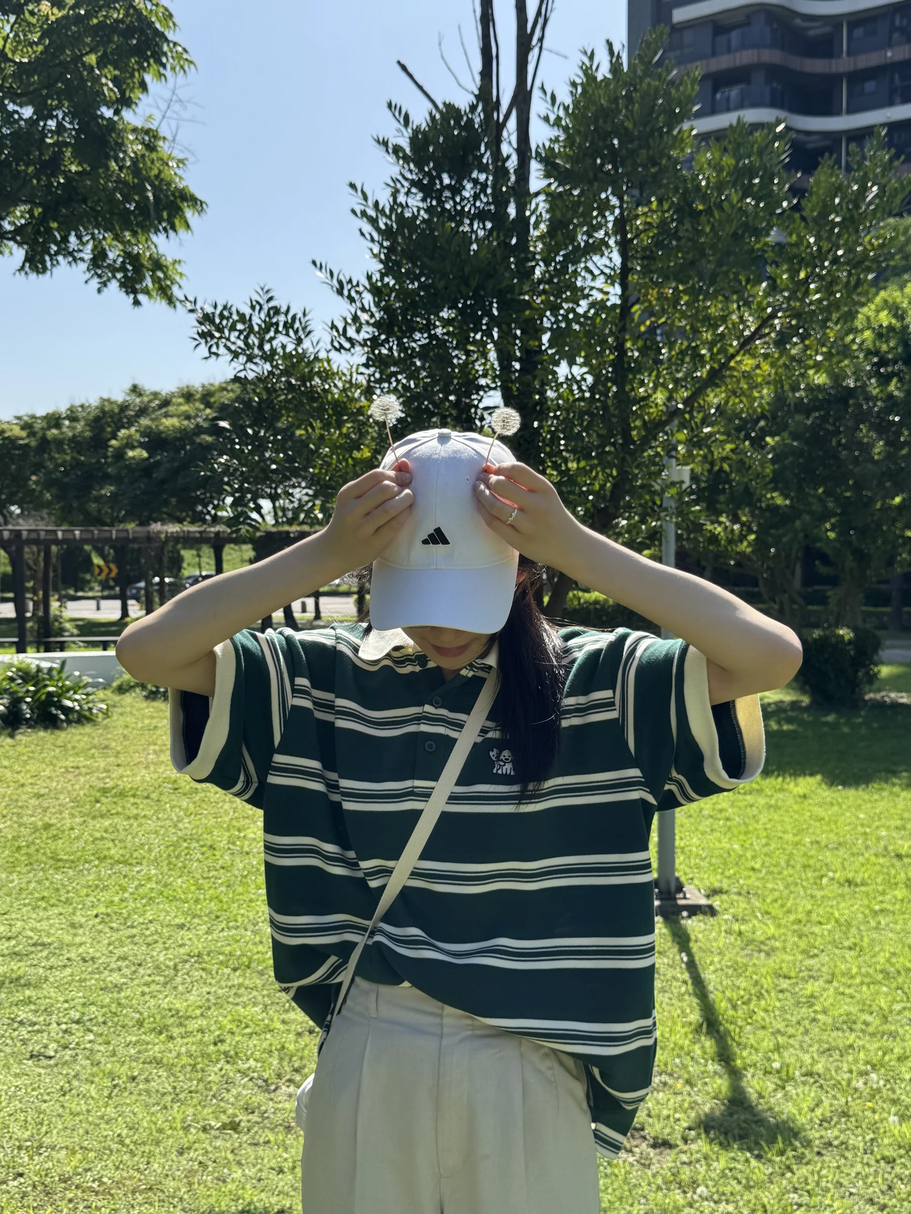 A person in a sunhat holds a striped garment open on a sunlit lawn.