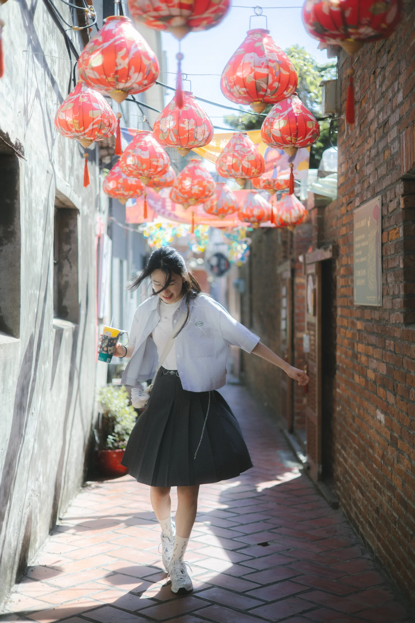 A person walks through a narrow lane beneath clusters of red lanterns.