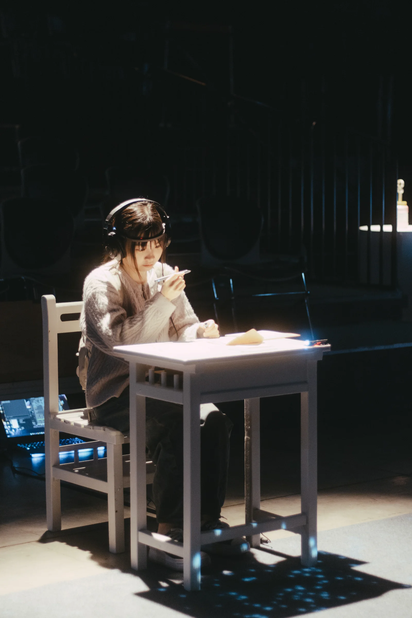 A performer leans over a desk beneath a pool of stage light.