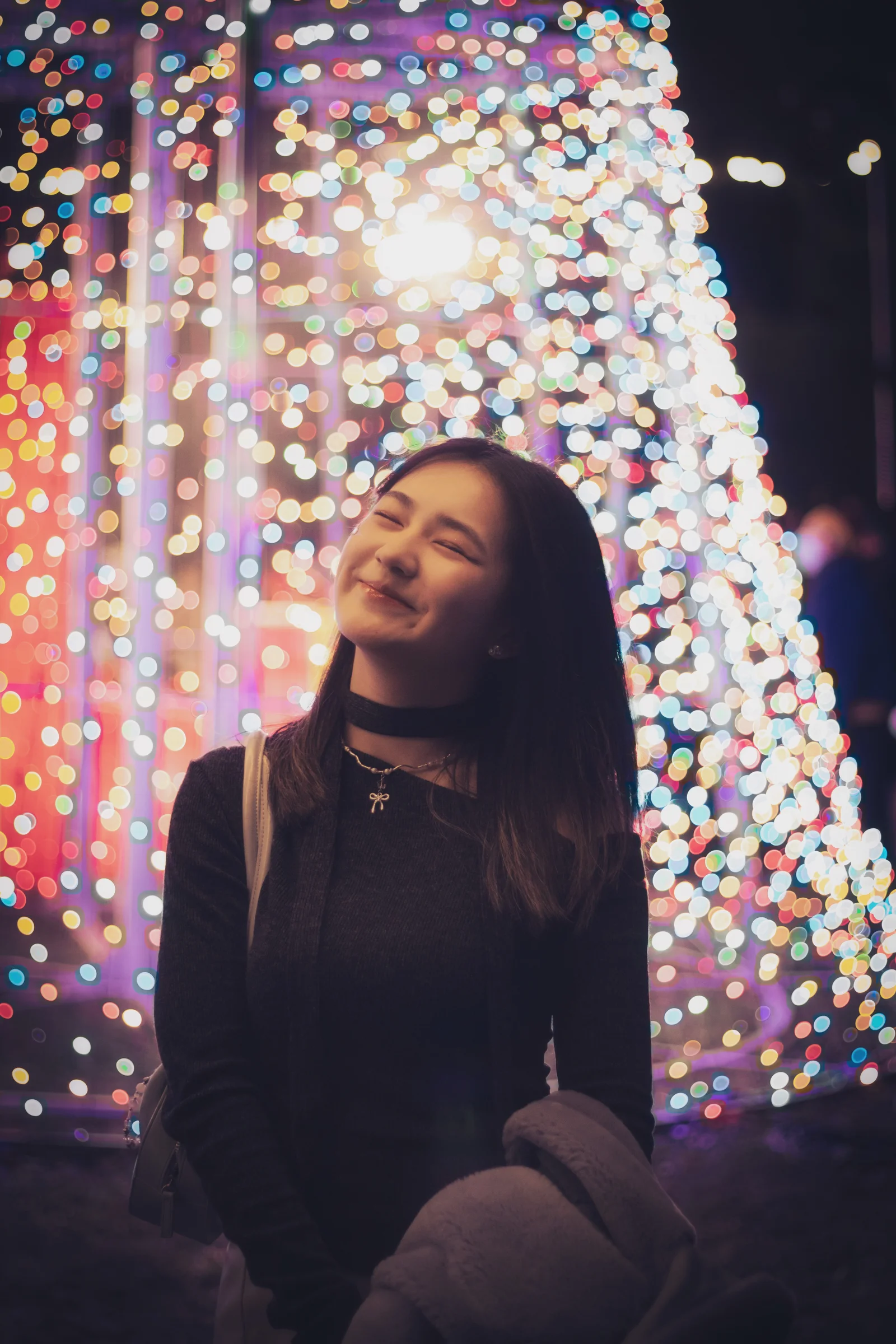 A person looks upward beside a curtain of colorful decorative lights at night.