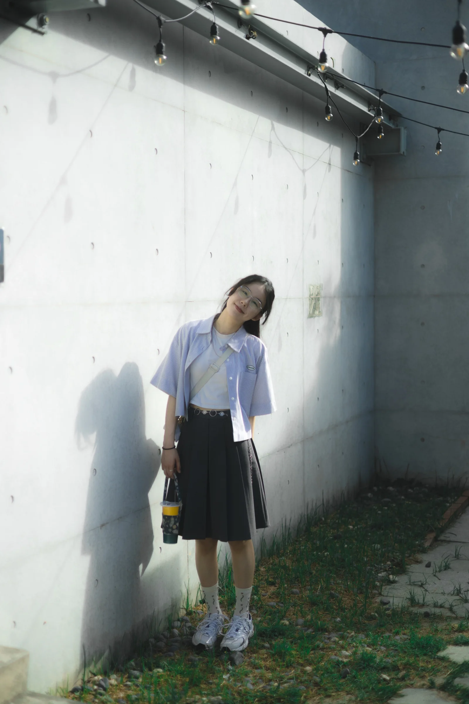 A person stands in sunlight along a weathered white wall beneath a tiled roof.