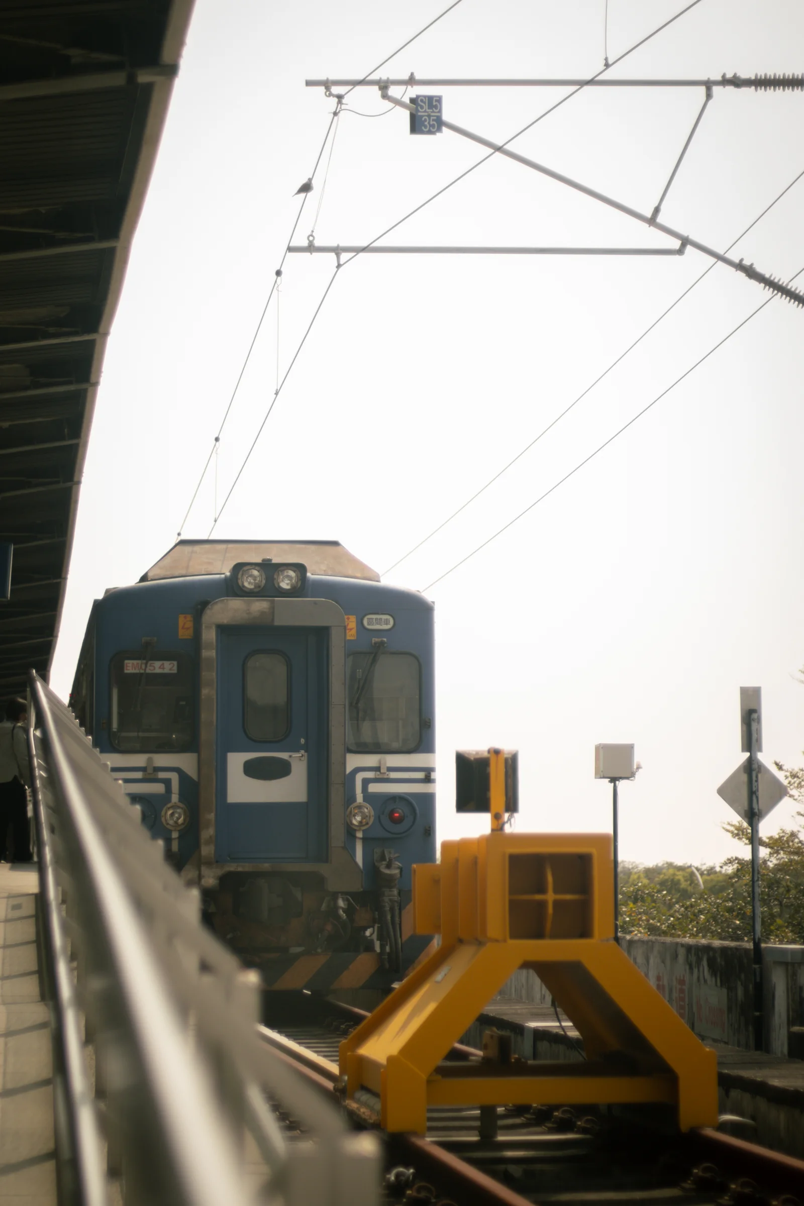 A train stands at the end of a track beneath overhead railway wires.