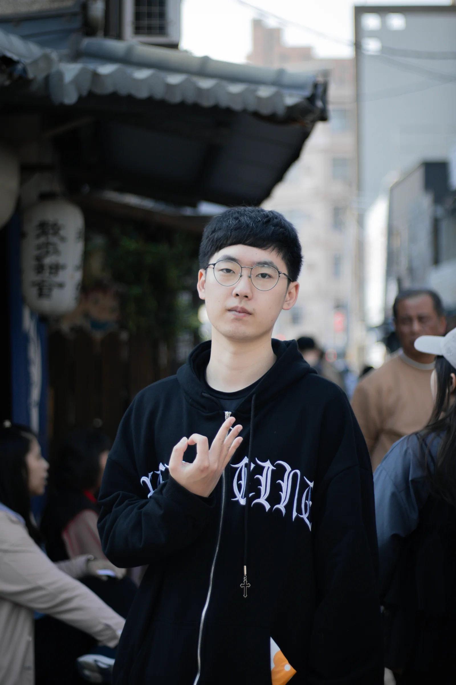 A person wearing glasses gestures while standing in a narrow street.