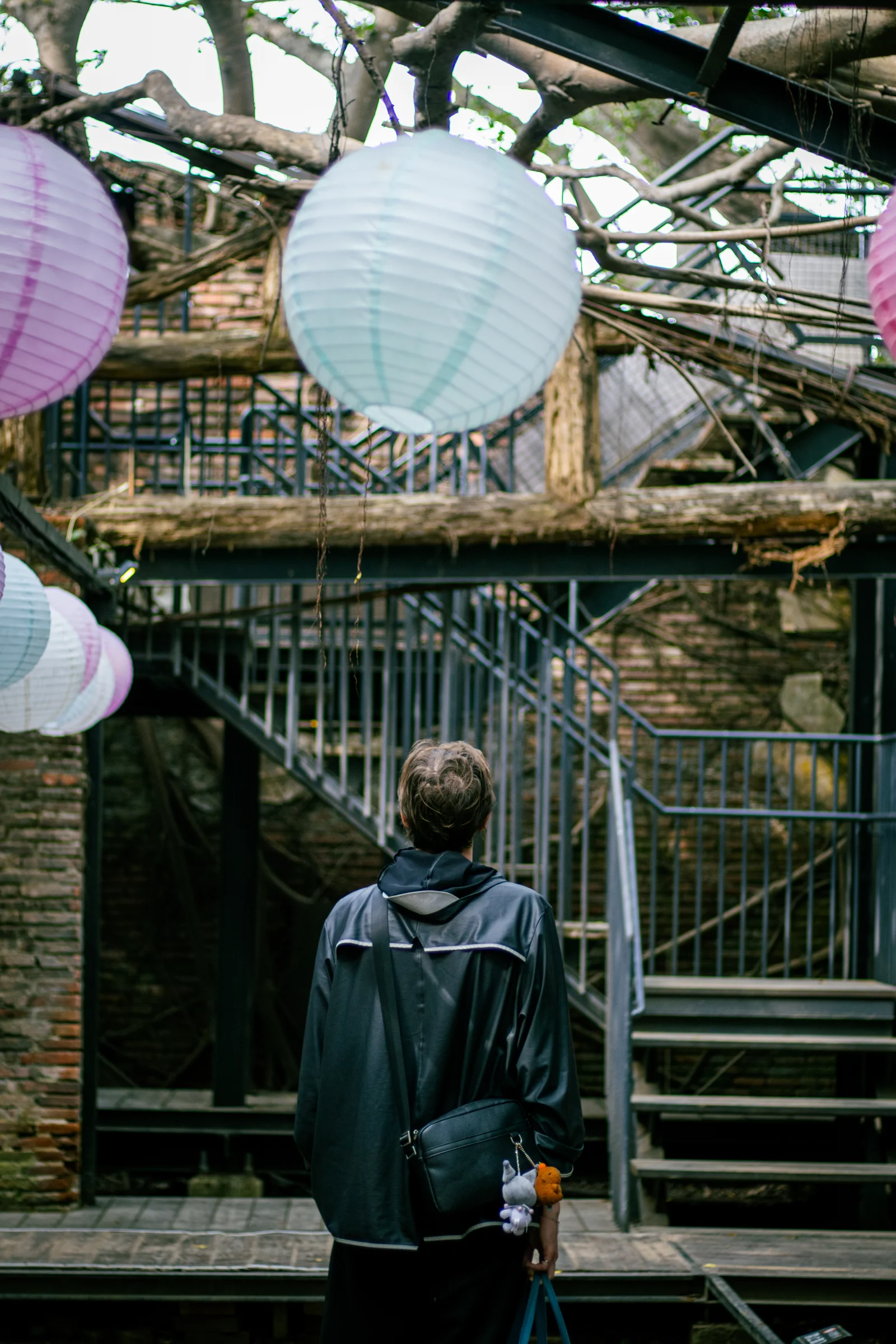 A person stands beneath pastel lanterns in front of a wooden building.