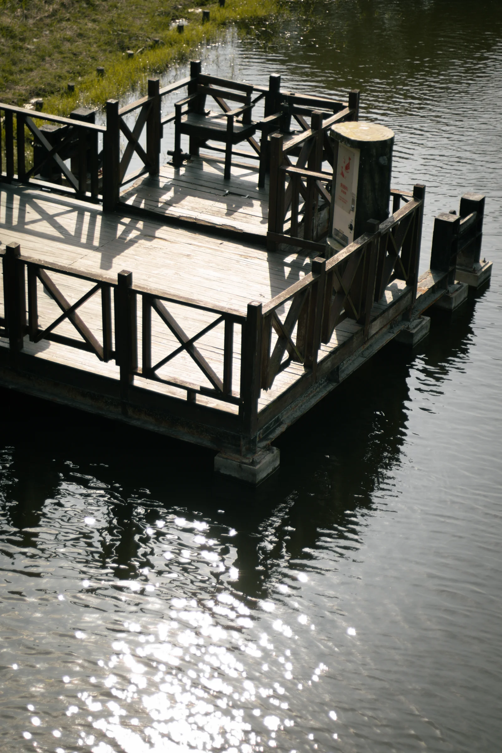 Sunlight sparkles on water beneath a small wooden platform and railings.