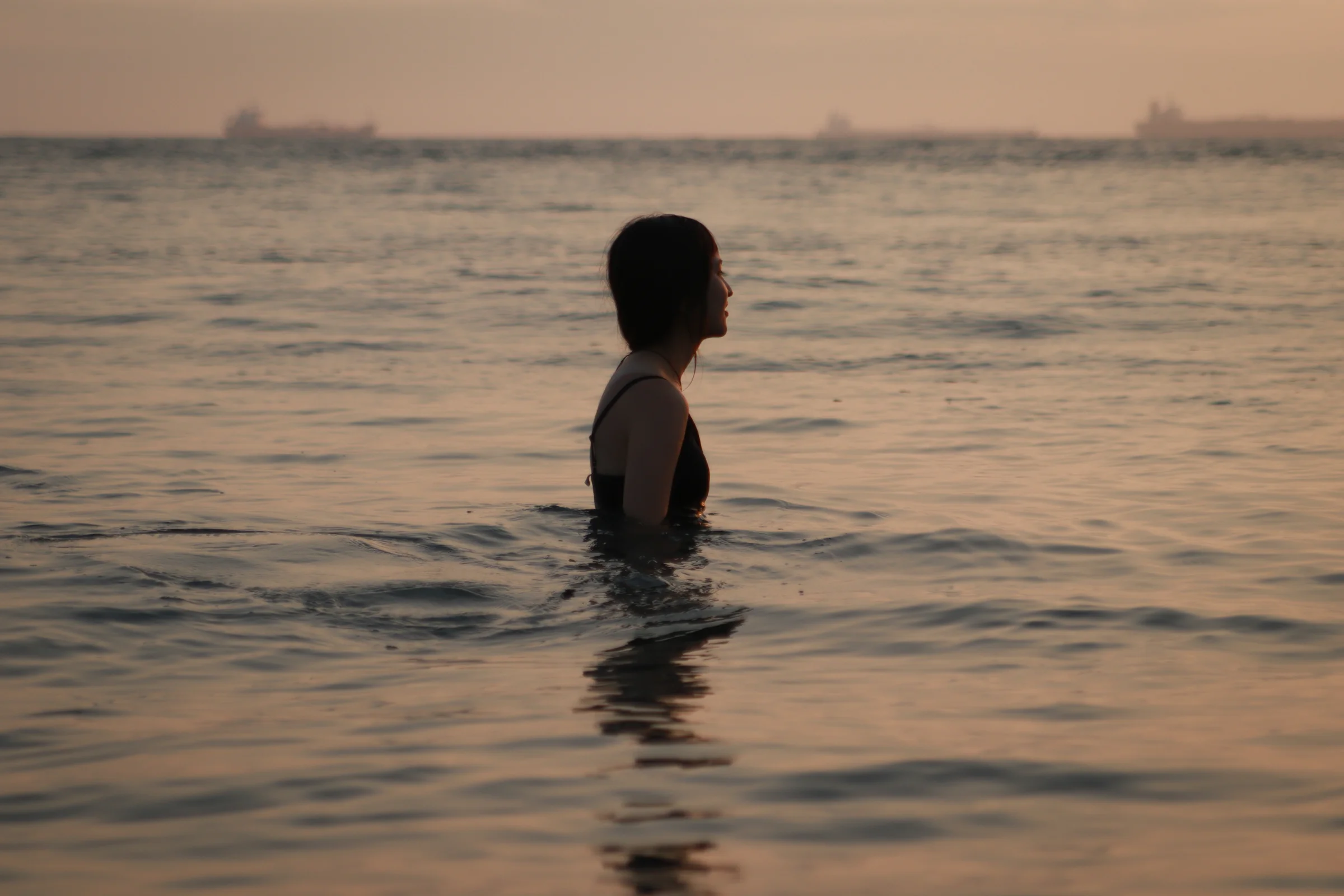 A swimmer is silhouetted against gentle sea waves beneath a warm evening sky.