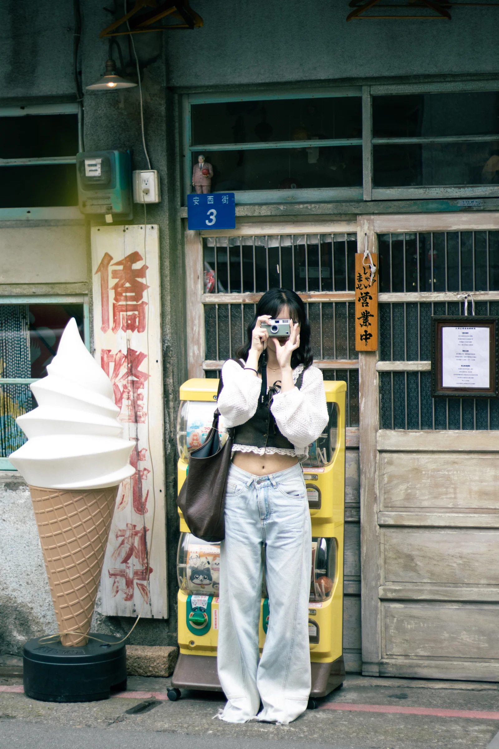 A person holding an ice cream stands outside a shop beside a large ice cream model.