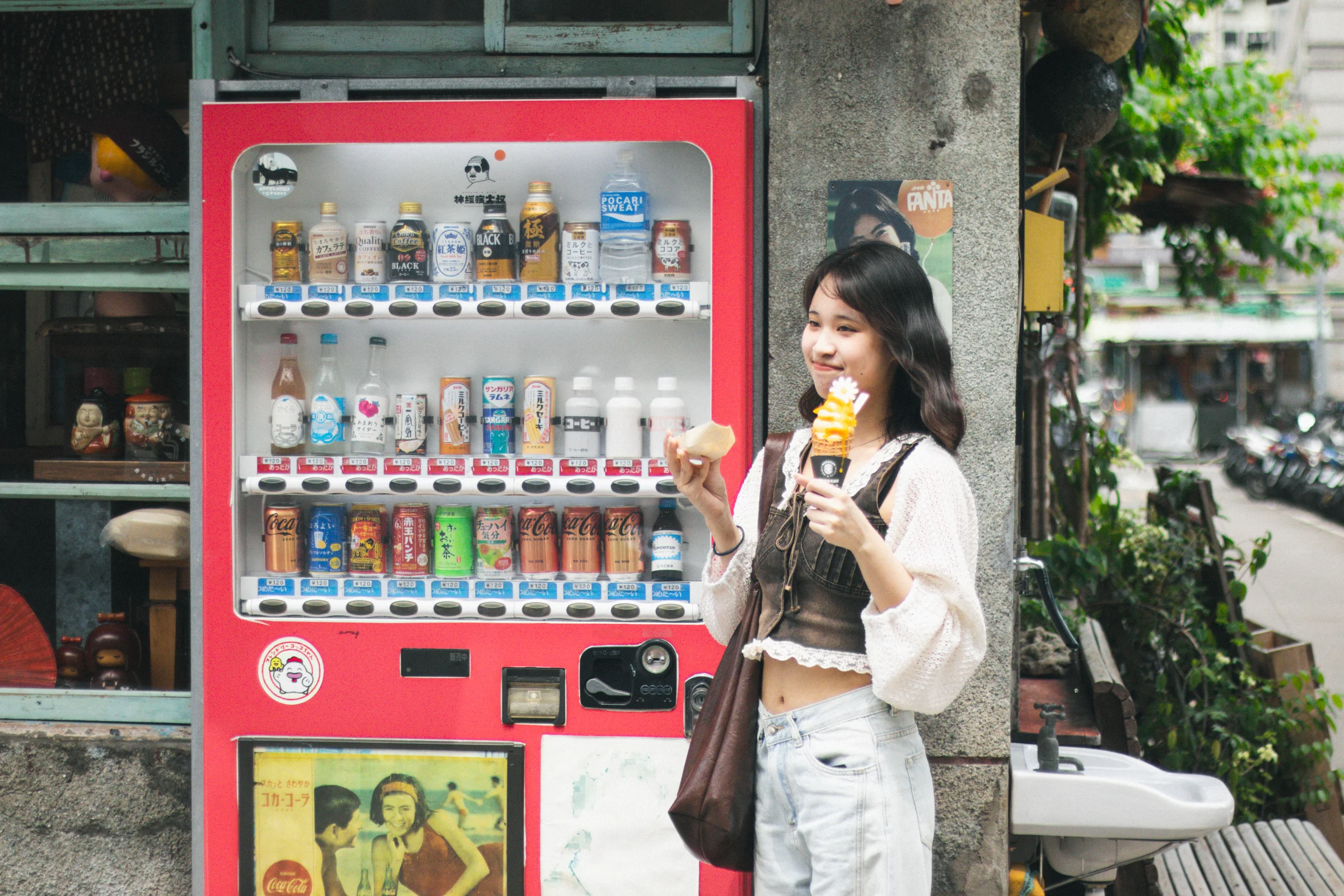 A person holding an ice cream stands beside a bright red vending machine.