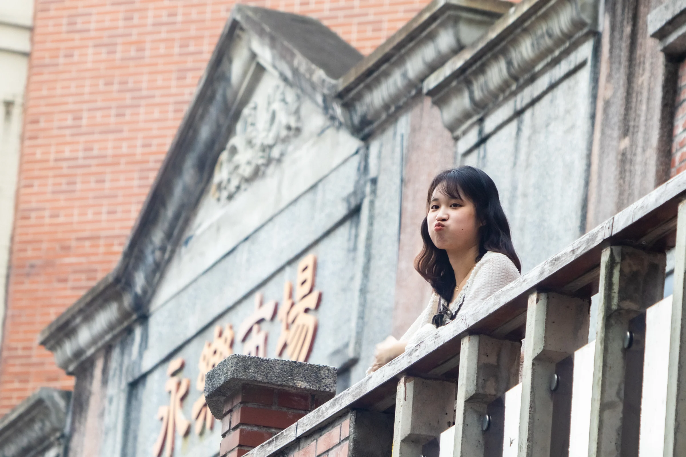 A person looks outward from a weathered balcony beside brick and plaster walls.