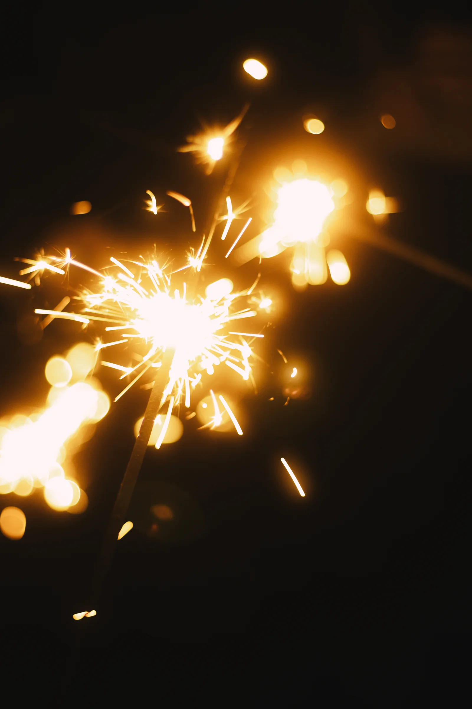 A sparkler scatters bright golden sparks against a dark background.