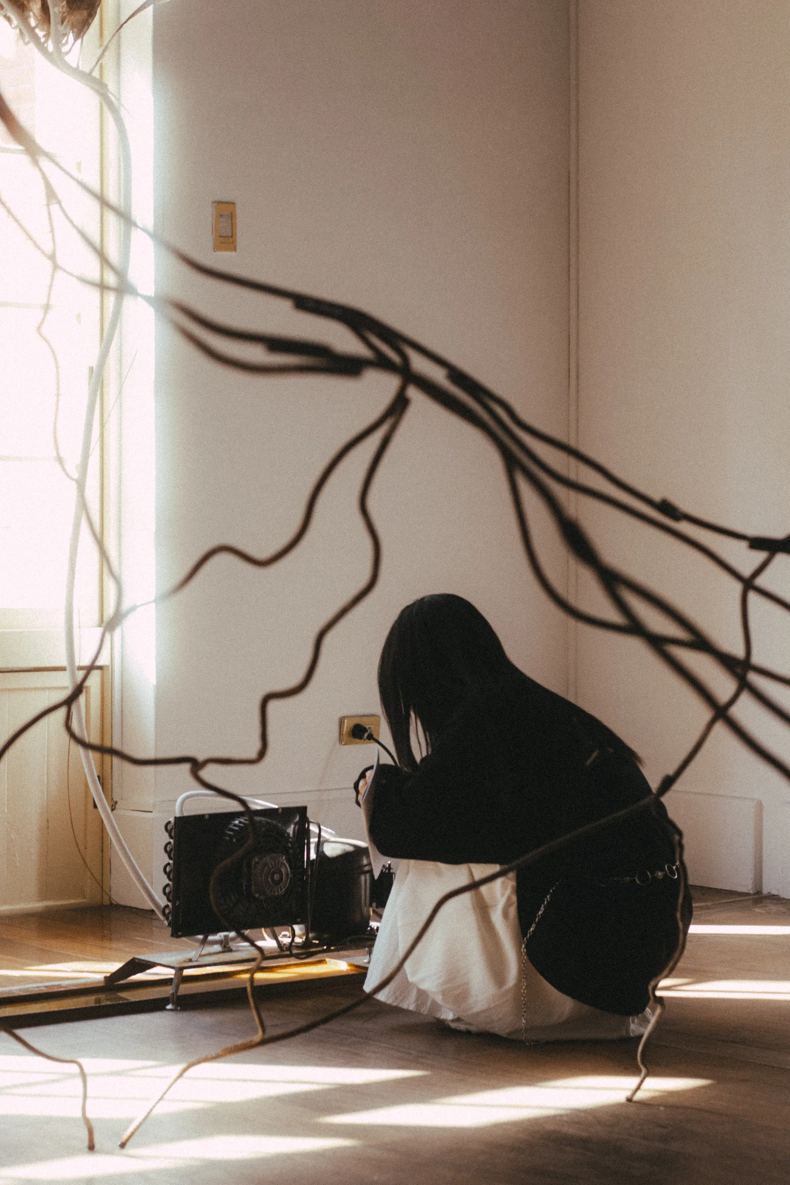 A person crouches beside a wall crossed by dark cables and a strong shadow.