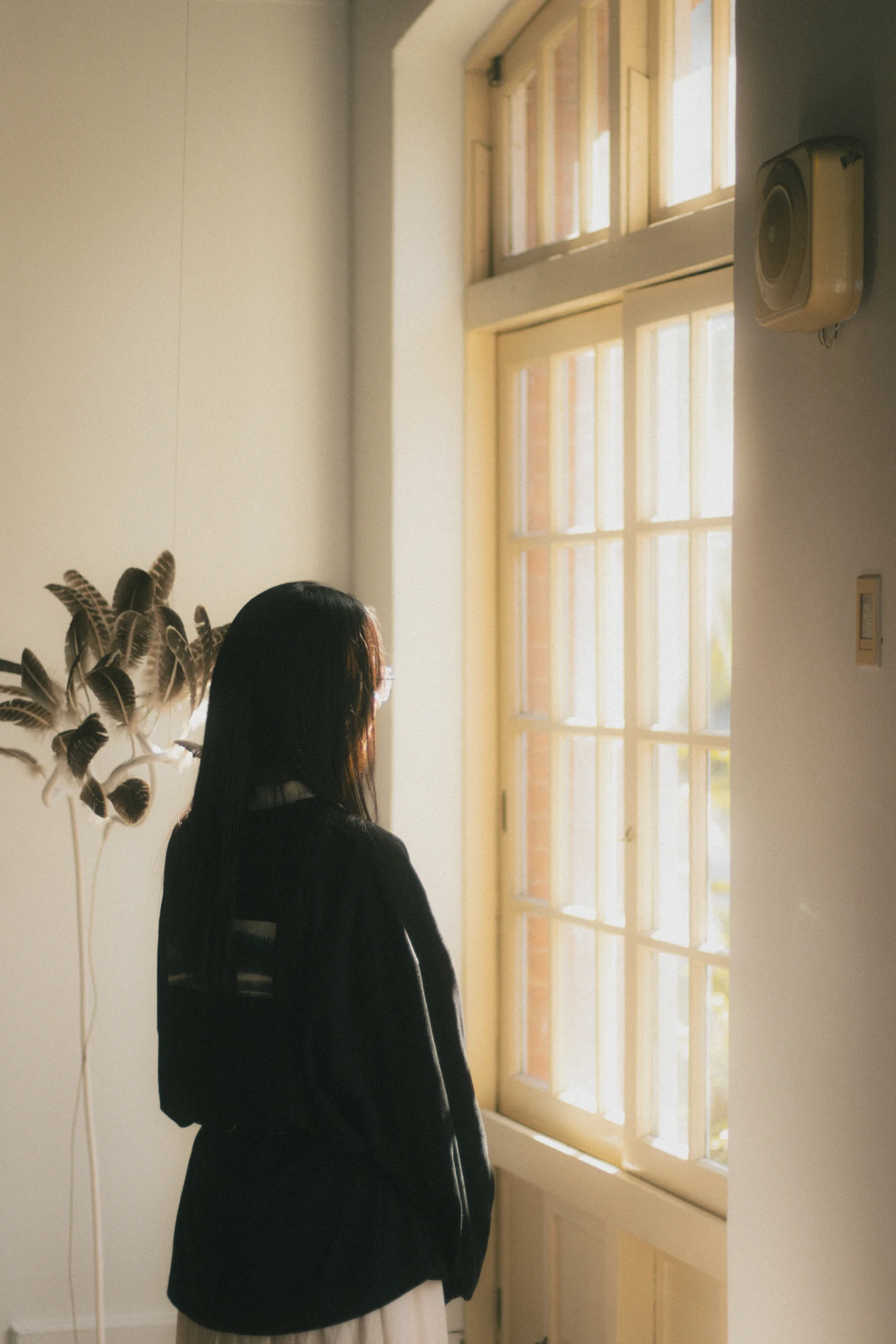 A person stands in silhouette beside a tall window glowing with warm daylight.