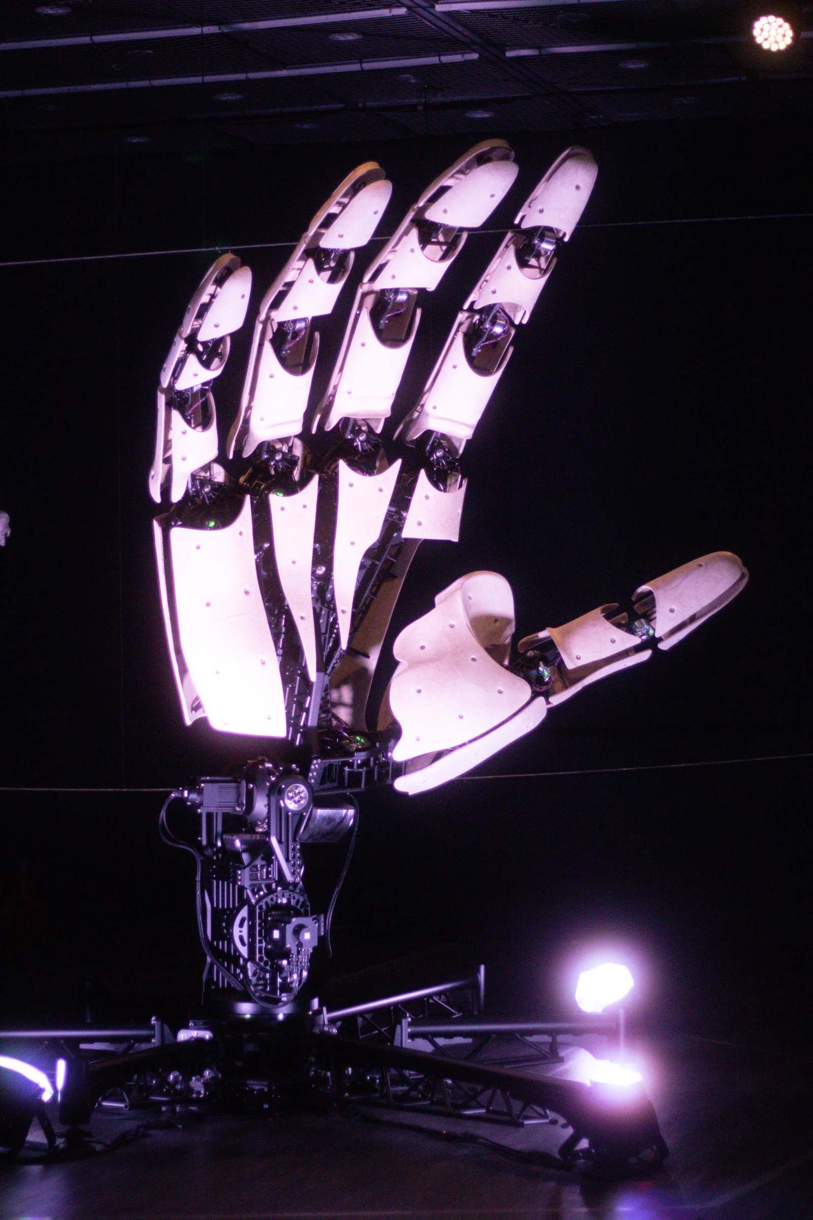 A large illuminated hand-shaped structure glows purple against a dark background.