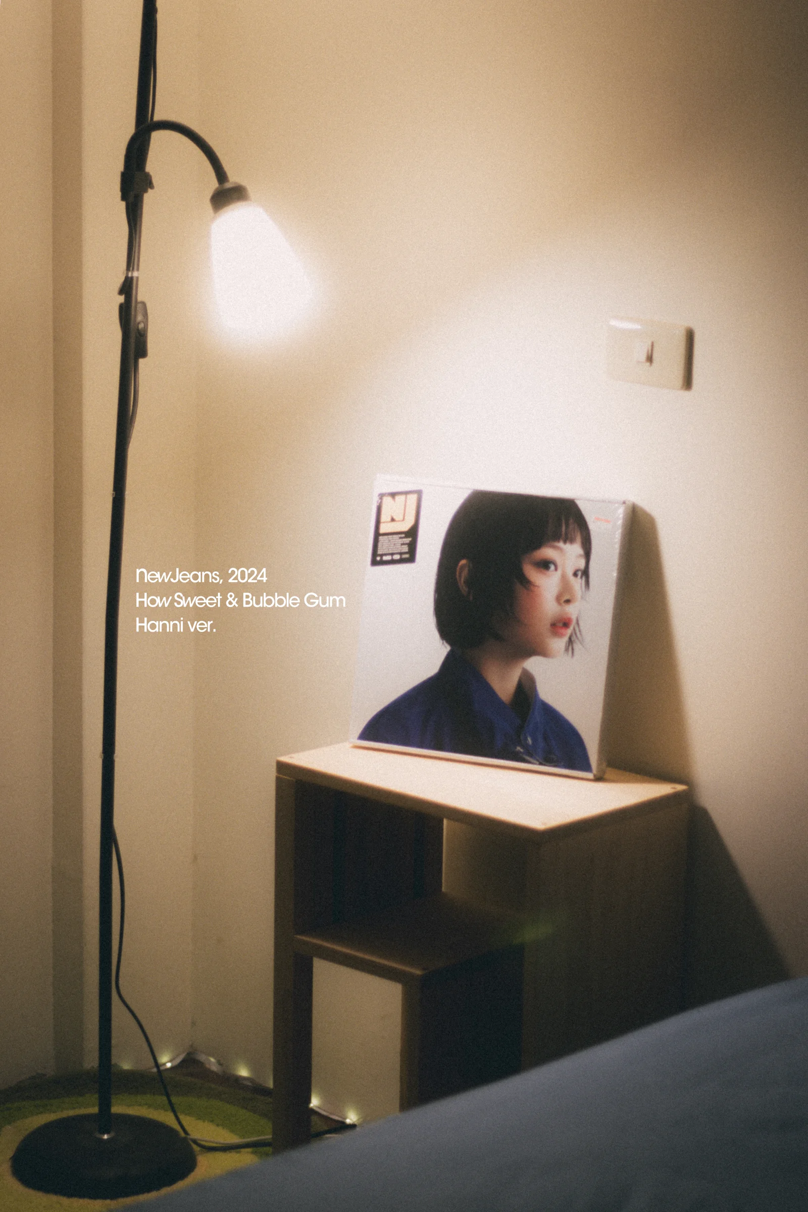 A warm-toned vertical composition shows a portrait on a monitor beside a hanging light bulb and a window.