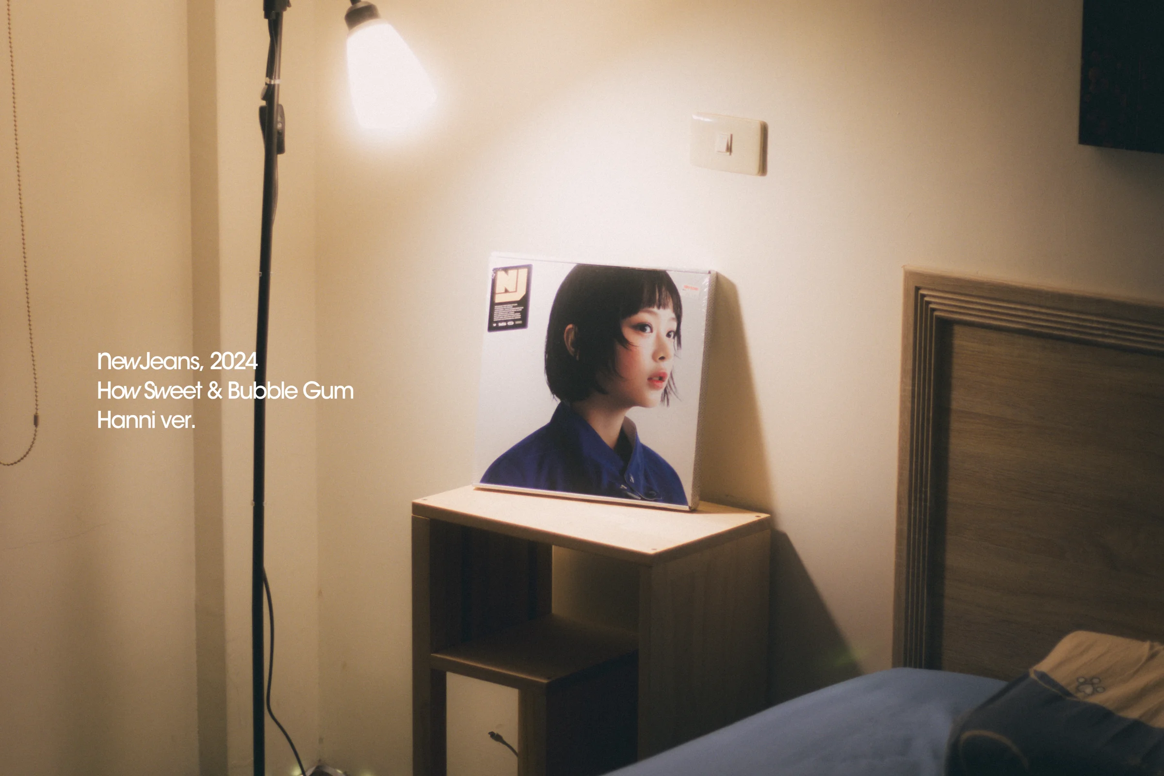 A warm-toned composition shows a portrait on a monitor, a hanging light bulb, a window, and small white text.