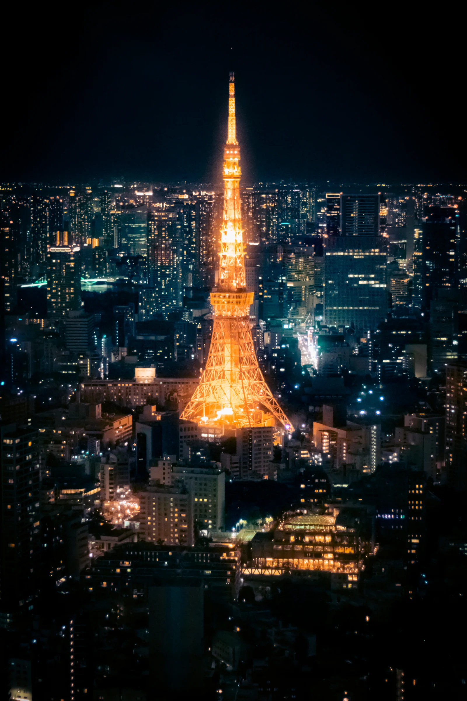 Tokyo Tower glows orange amid a dense city skyline at night.