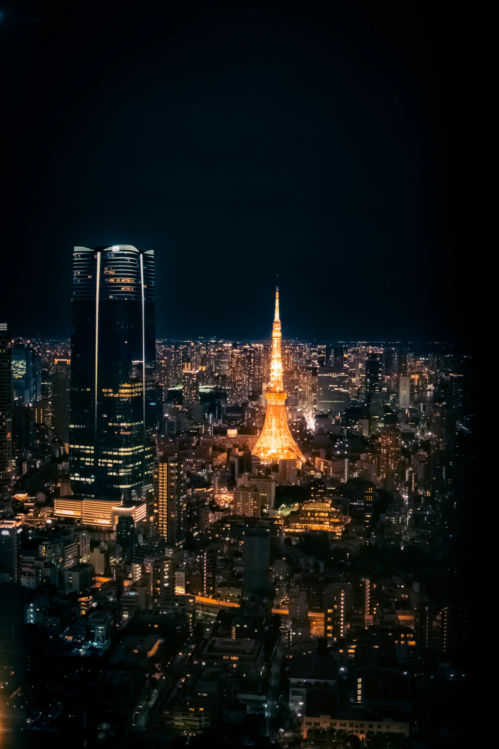 An illuminated Tokyo Tower stands among buildings and city lights at night.