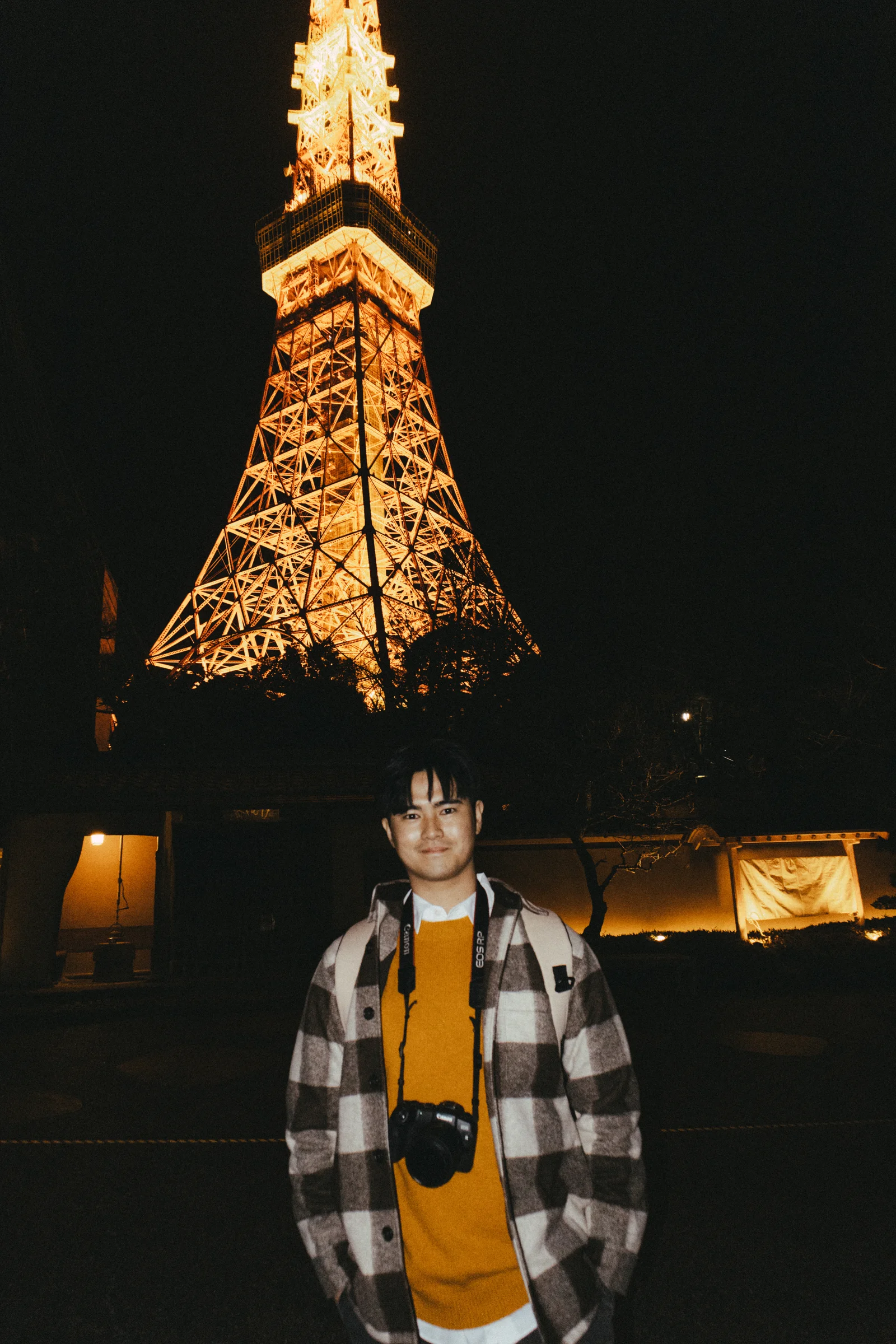 A person poses beneath the illuminated steel structure of Tokyo Tower.