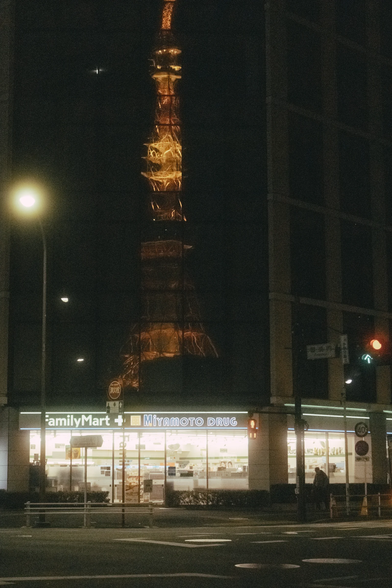 Tokyo Tower appears above a brightly lit street corner at night.