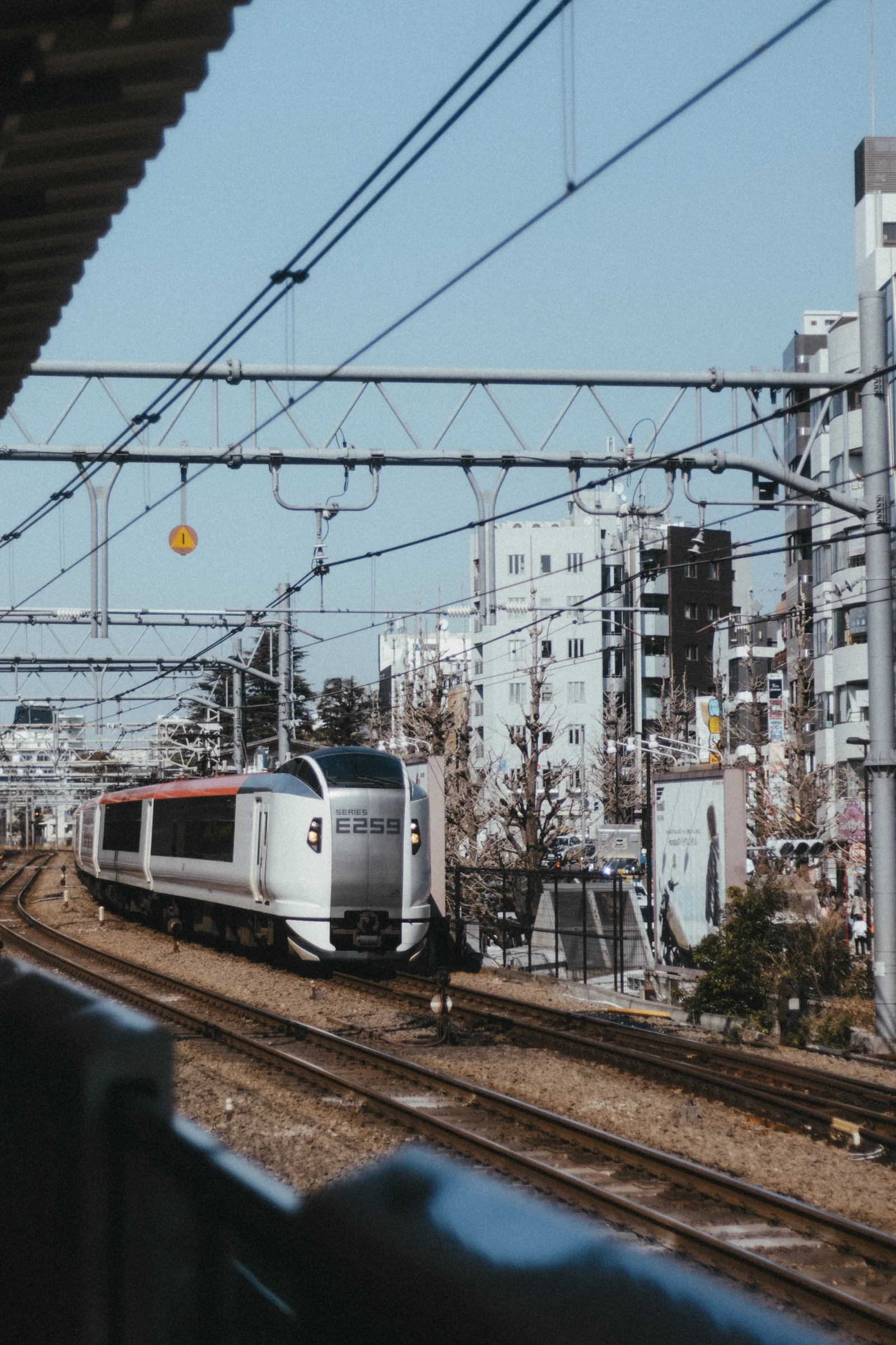 A commuter train follows tracks beneath overhead wires in a residential neighborhood.