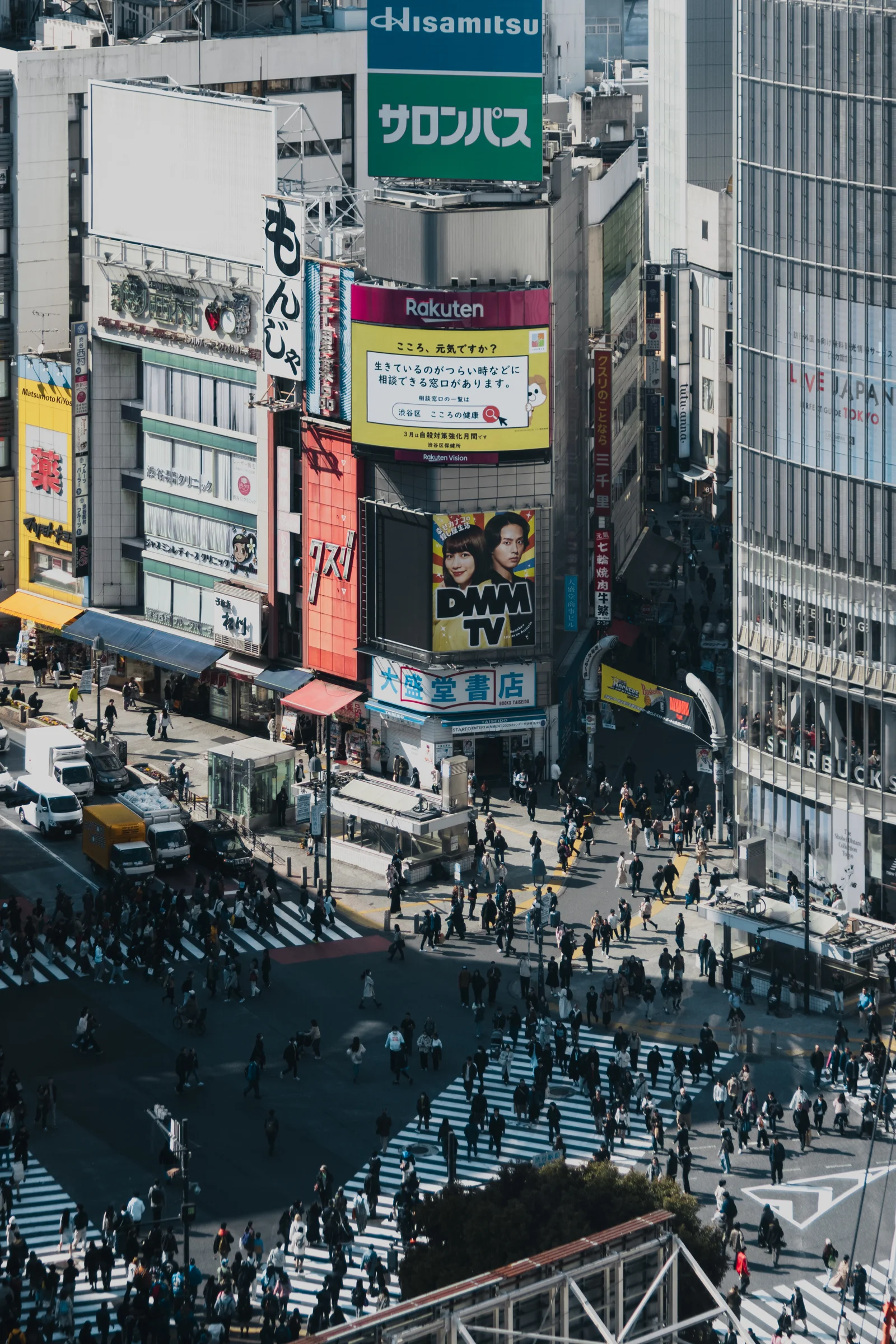 Crowds cross a famous intersection at Shibuya surrounded by tall buildings and colorful signs.