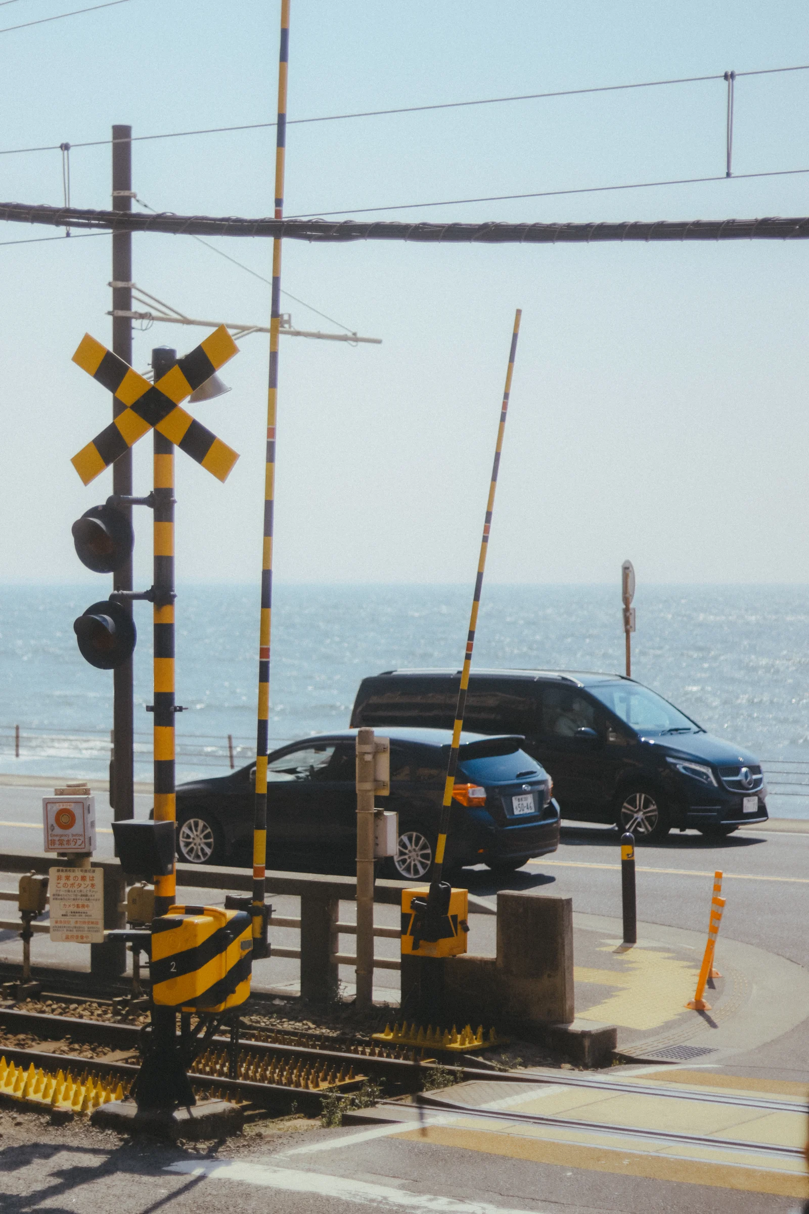 A railway crossing and a car sit beside the sparkling sea.