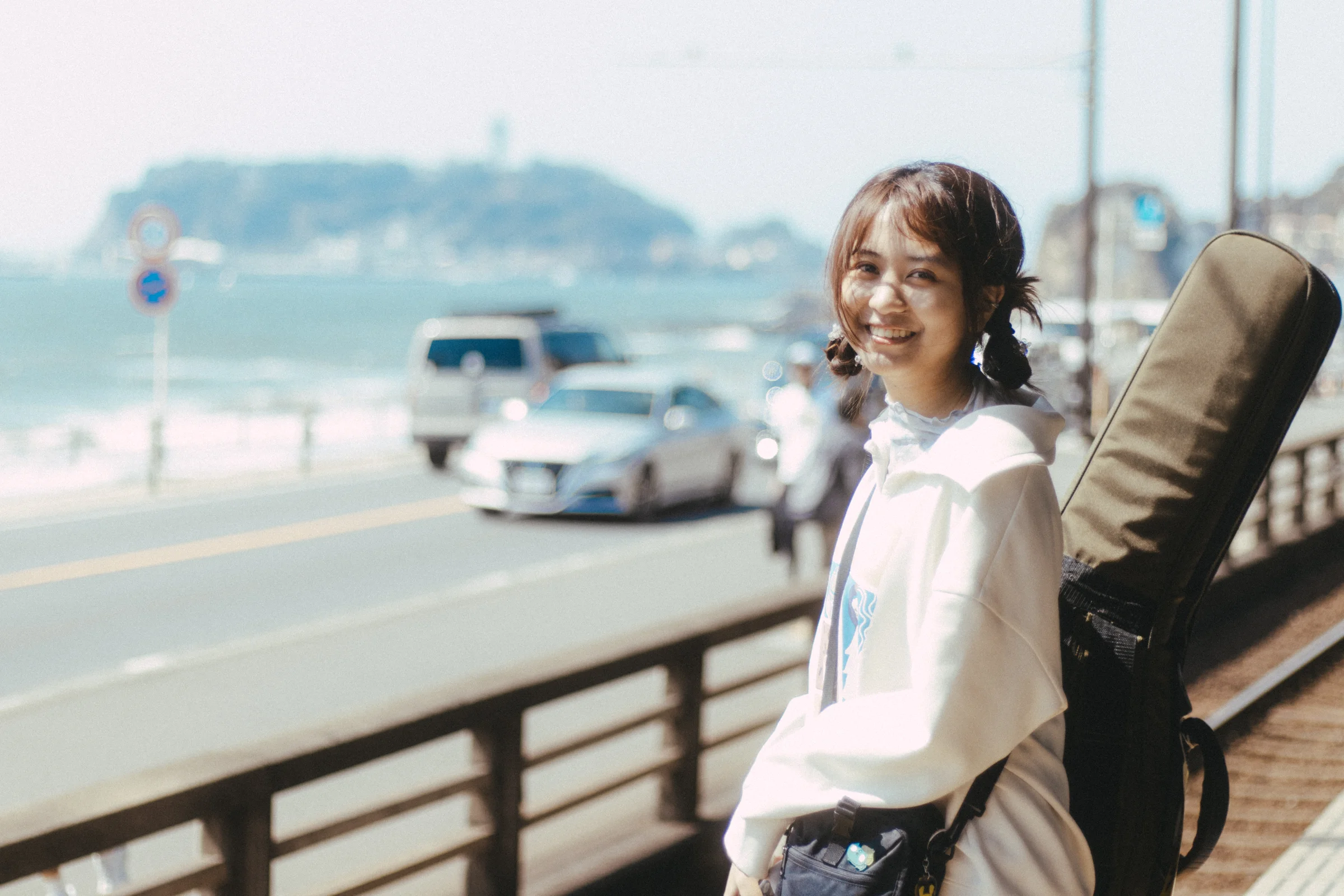 A person stands beside a coastal road with the sea and an island behind them.