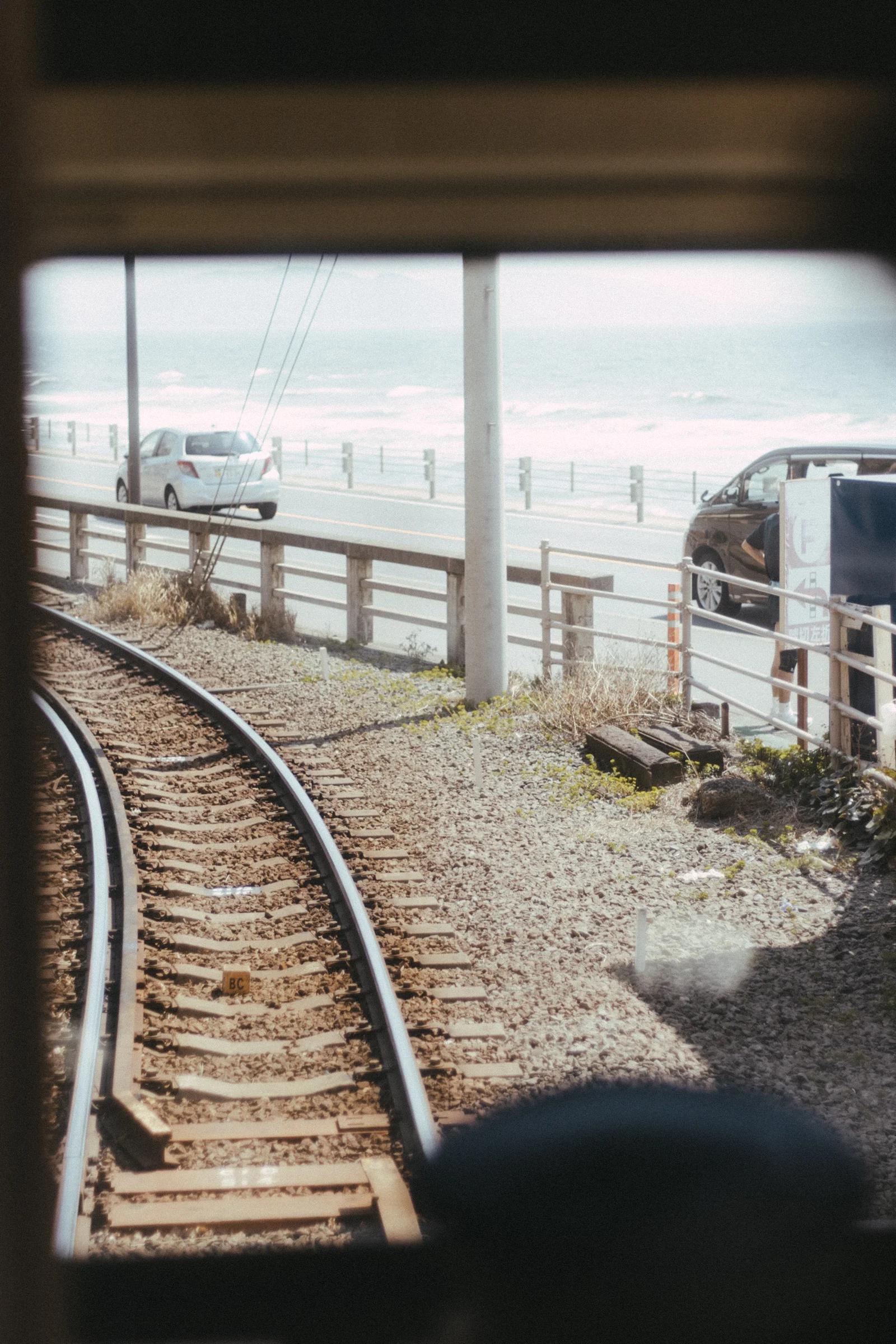Railway tracks curve past a train and buildings near the coast.
