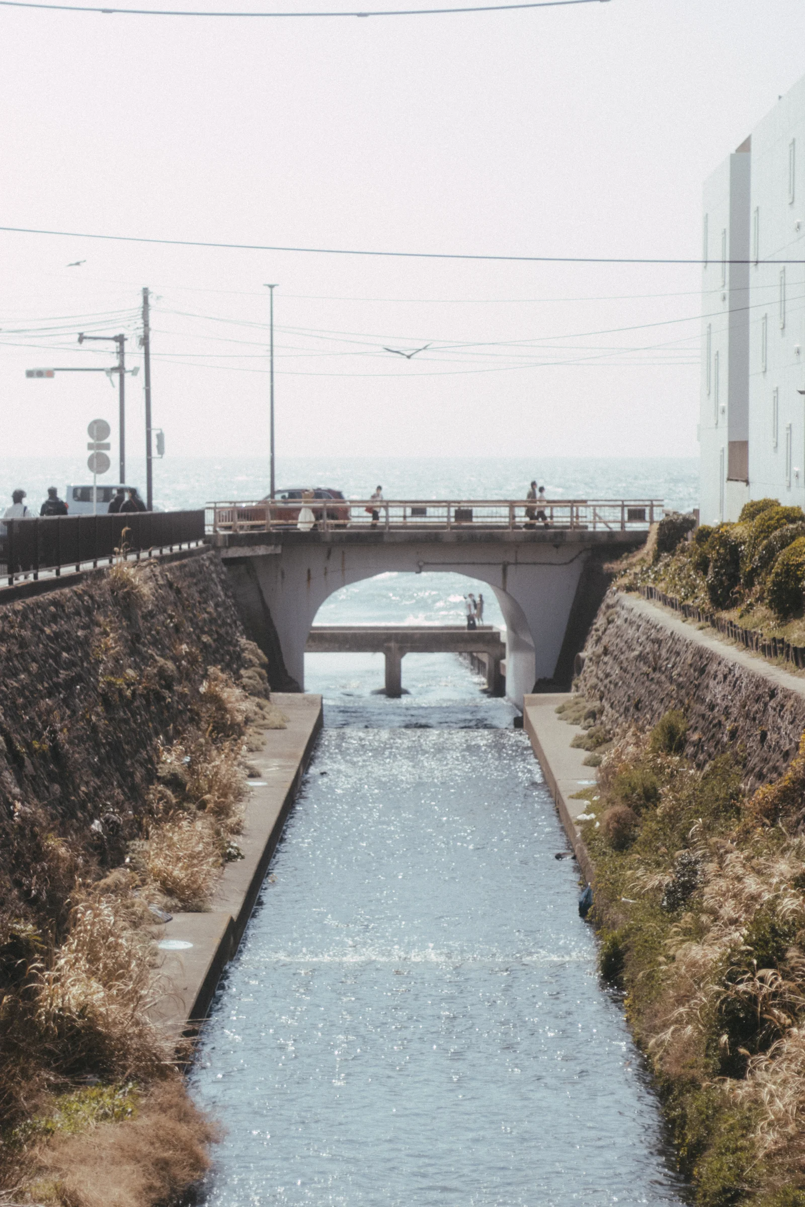A narrow channel runs beneath a small bridge toward the sea.