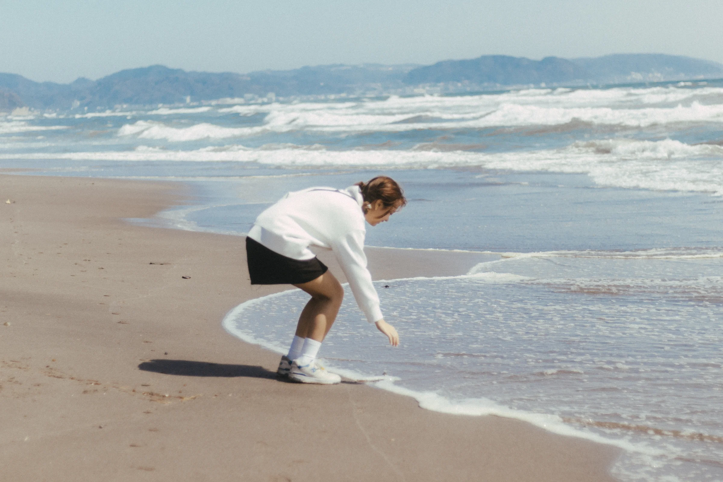 A person bends toward the water as a wave reaches the sandy beach.