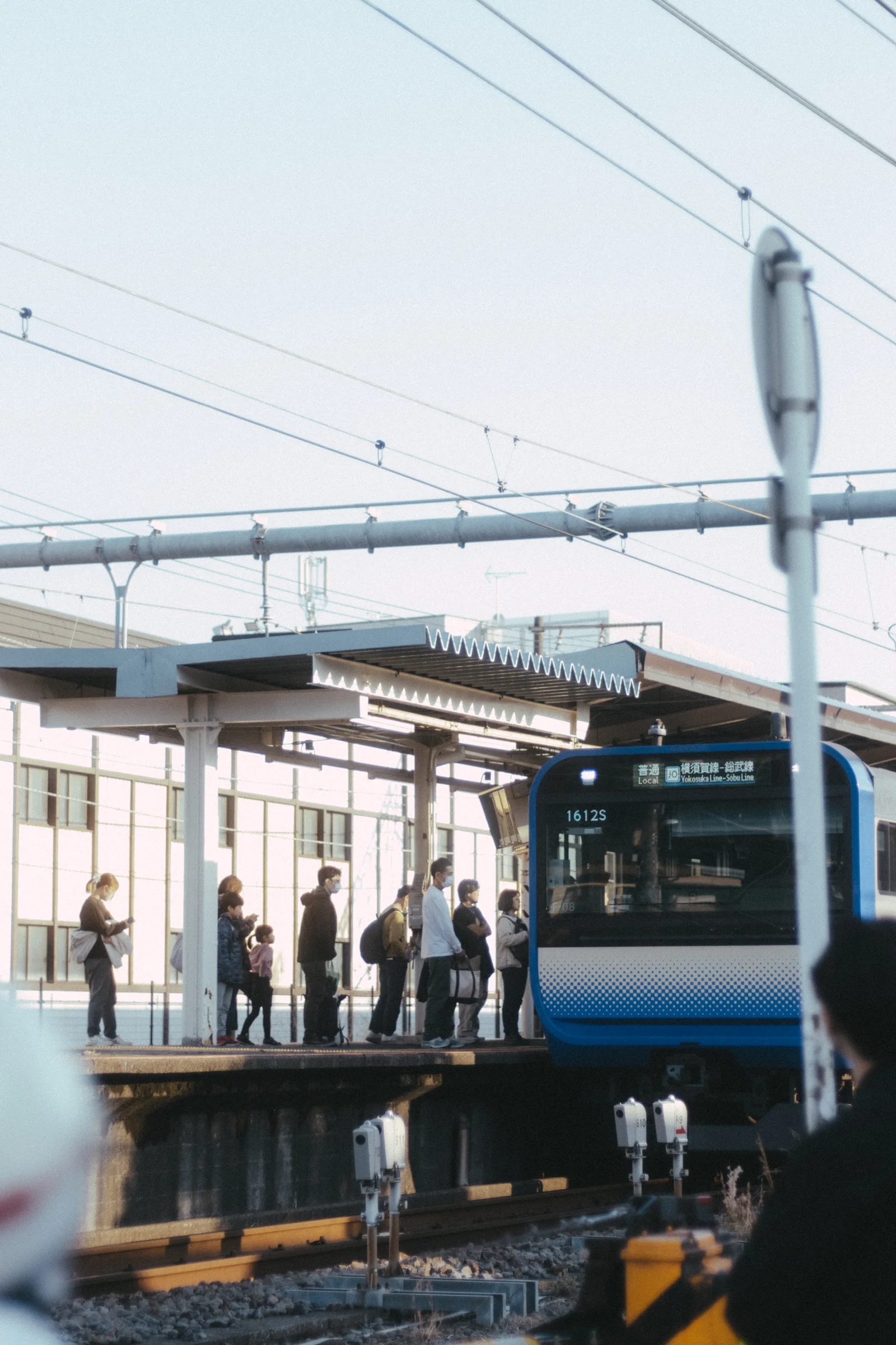 A blue-striped commuter train stands beside a station platform beneath overhead wires.