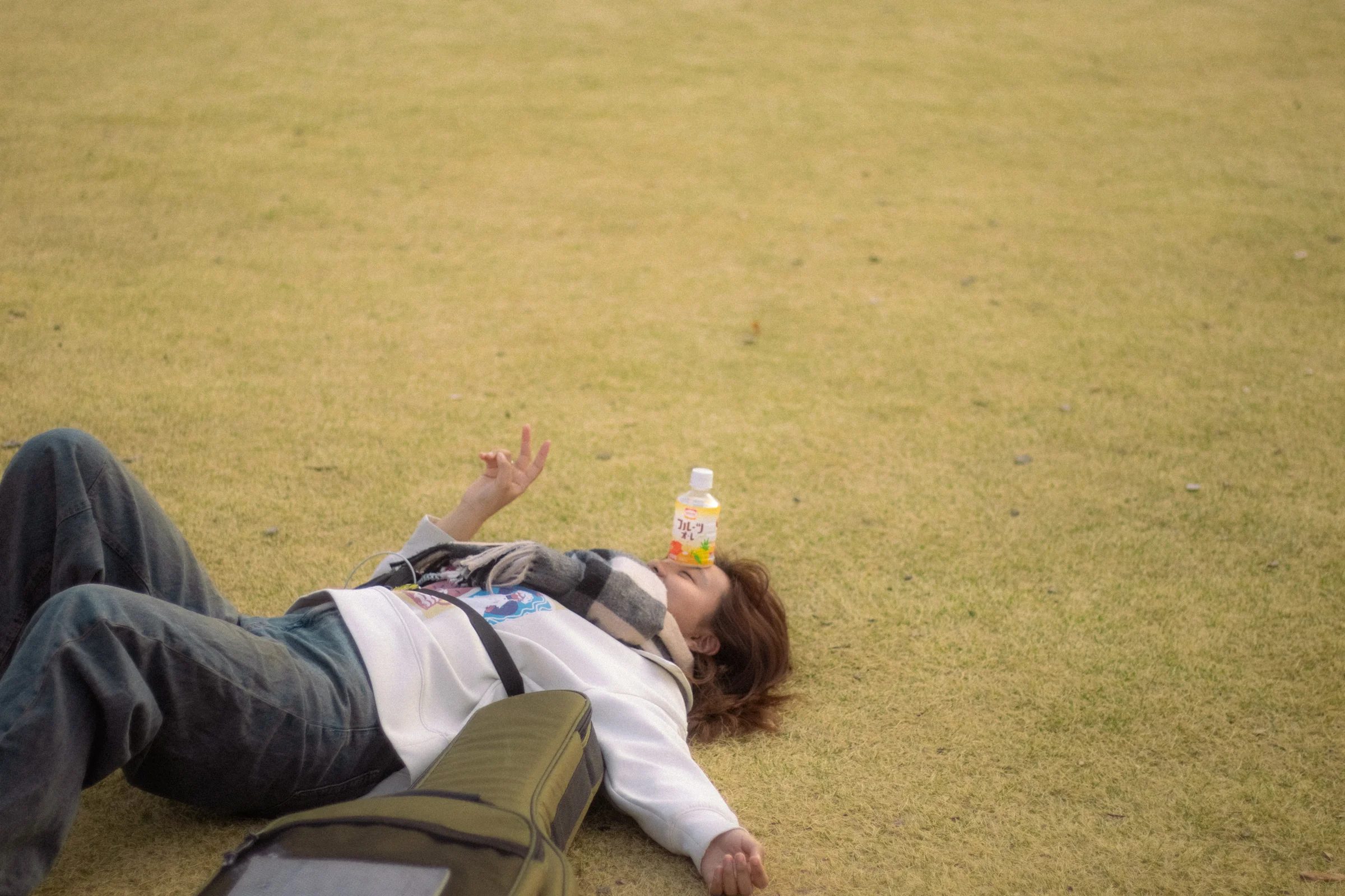 A person lies on sunlit grass with an arm across their face.