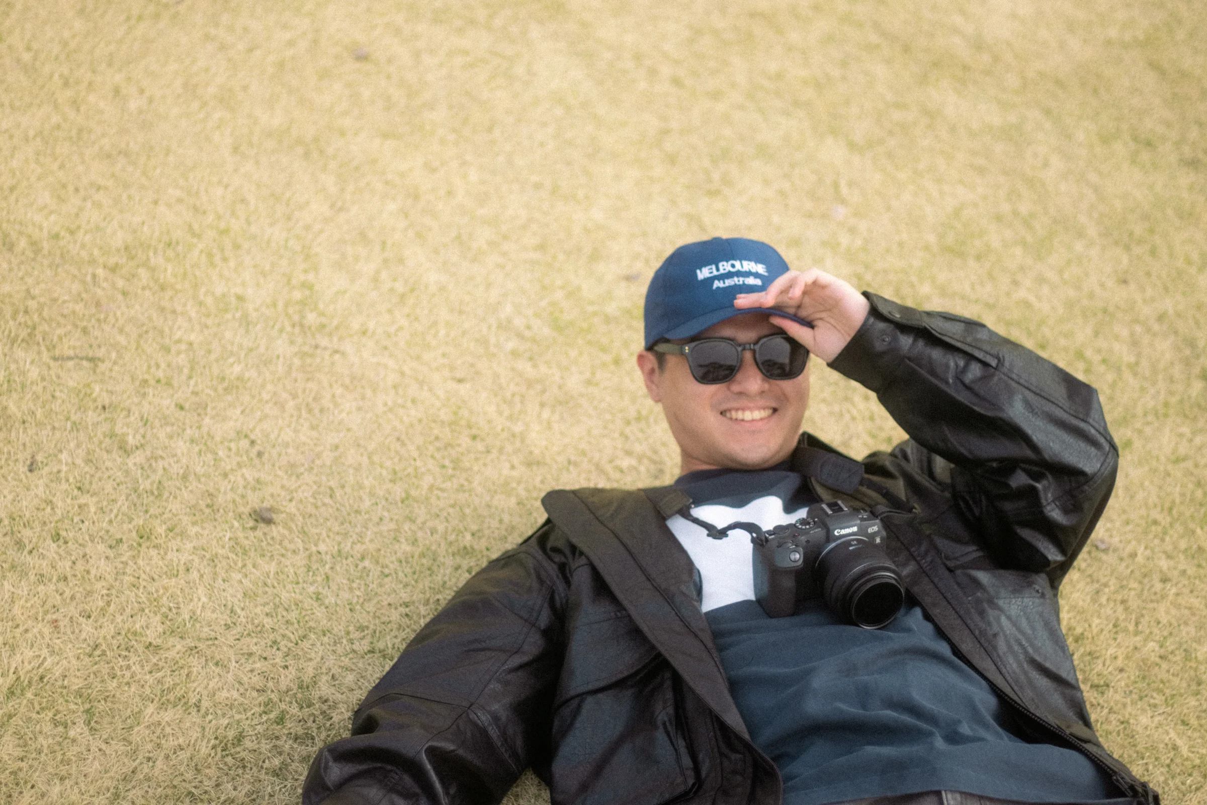A person in a dark jacket and cap rests on a golden lawn.